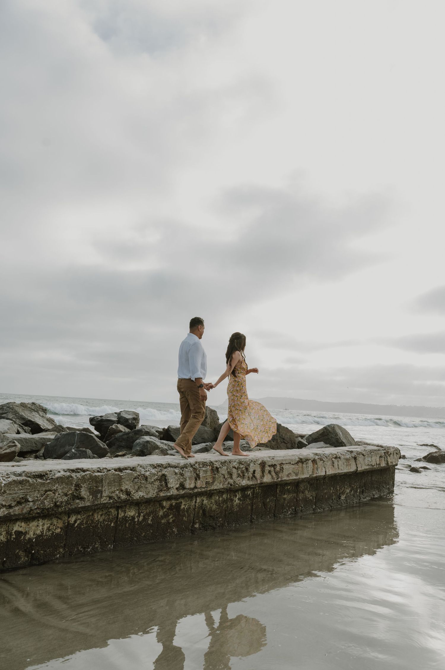 Couple sitting on a concrete pier overlooking the ocean on a cloudy day.