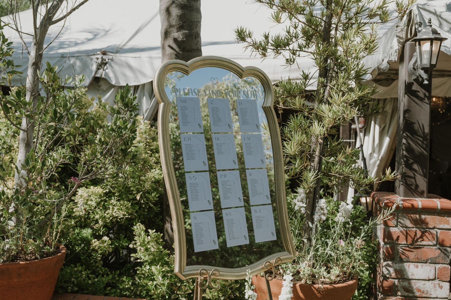 Elegant mirrored wedding seating chart sign displayed outdoors among lush green plants and foliage.