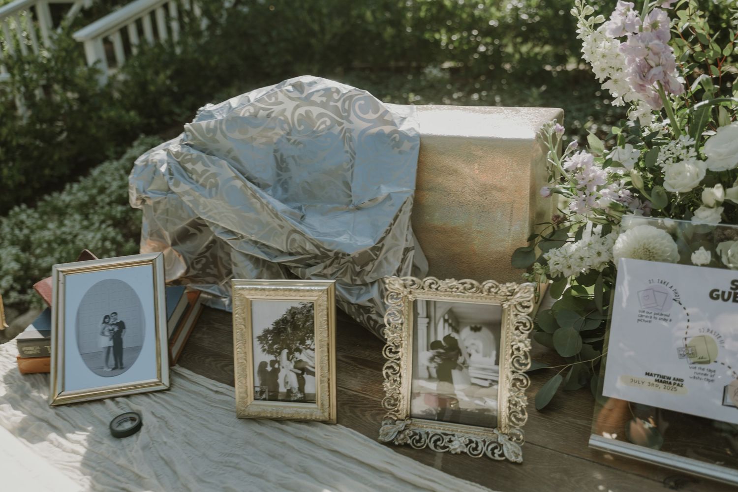 Vintage wedding memory table with framed black and white photos, antique frames, and floral arrangements on a wooden deck.