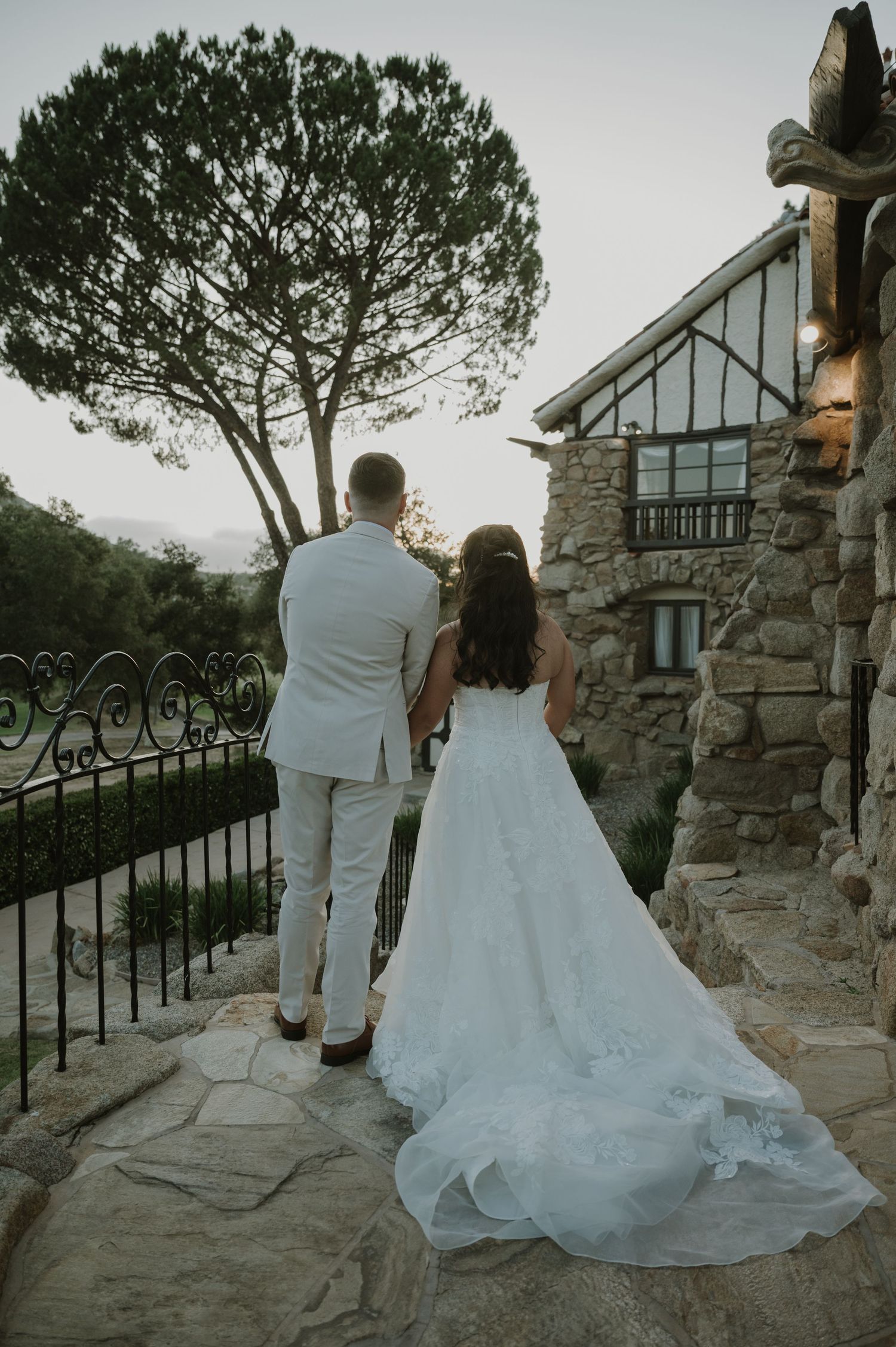 Bride and groom stand together viewing sunset at stone venue.