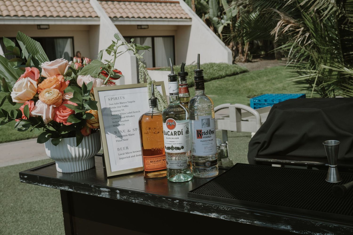 Wedding bar setup with liquor bottles and floral decorations on dark surface.