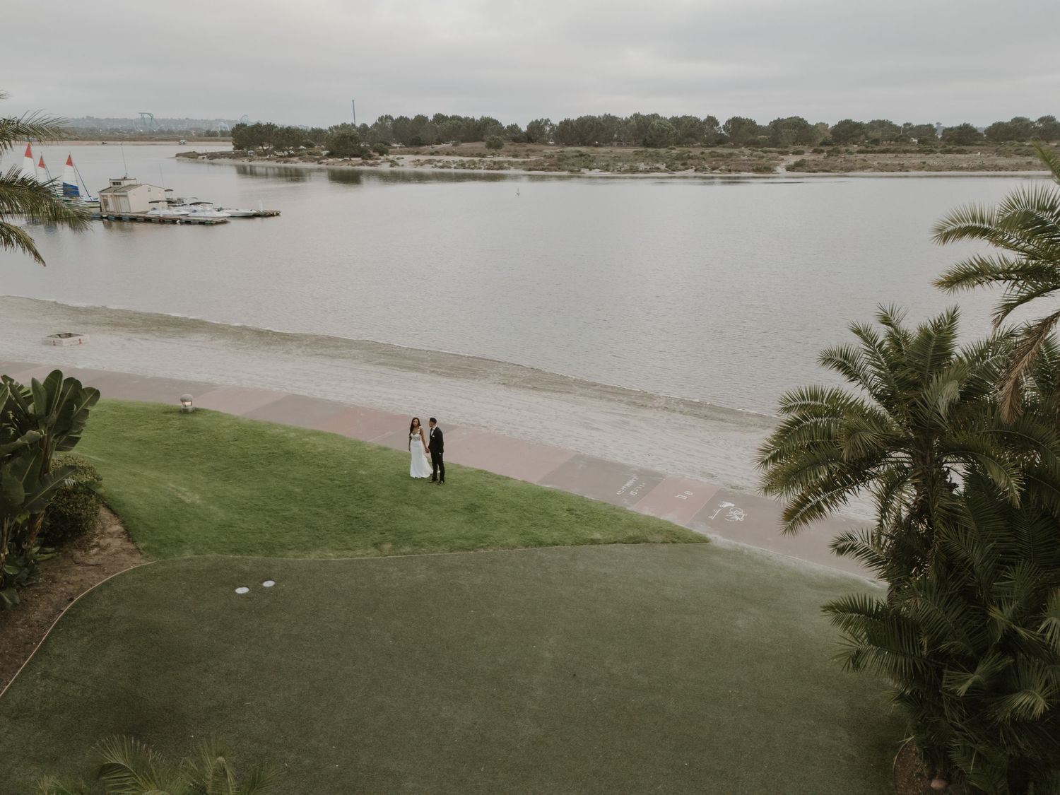 Panoramic view of a waterfront venue with palm trees and distant figures on the beach.