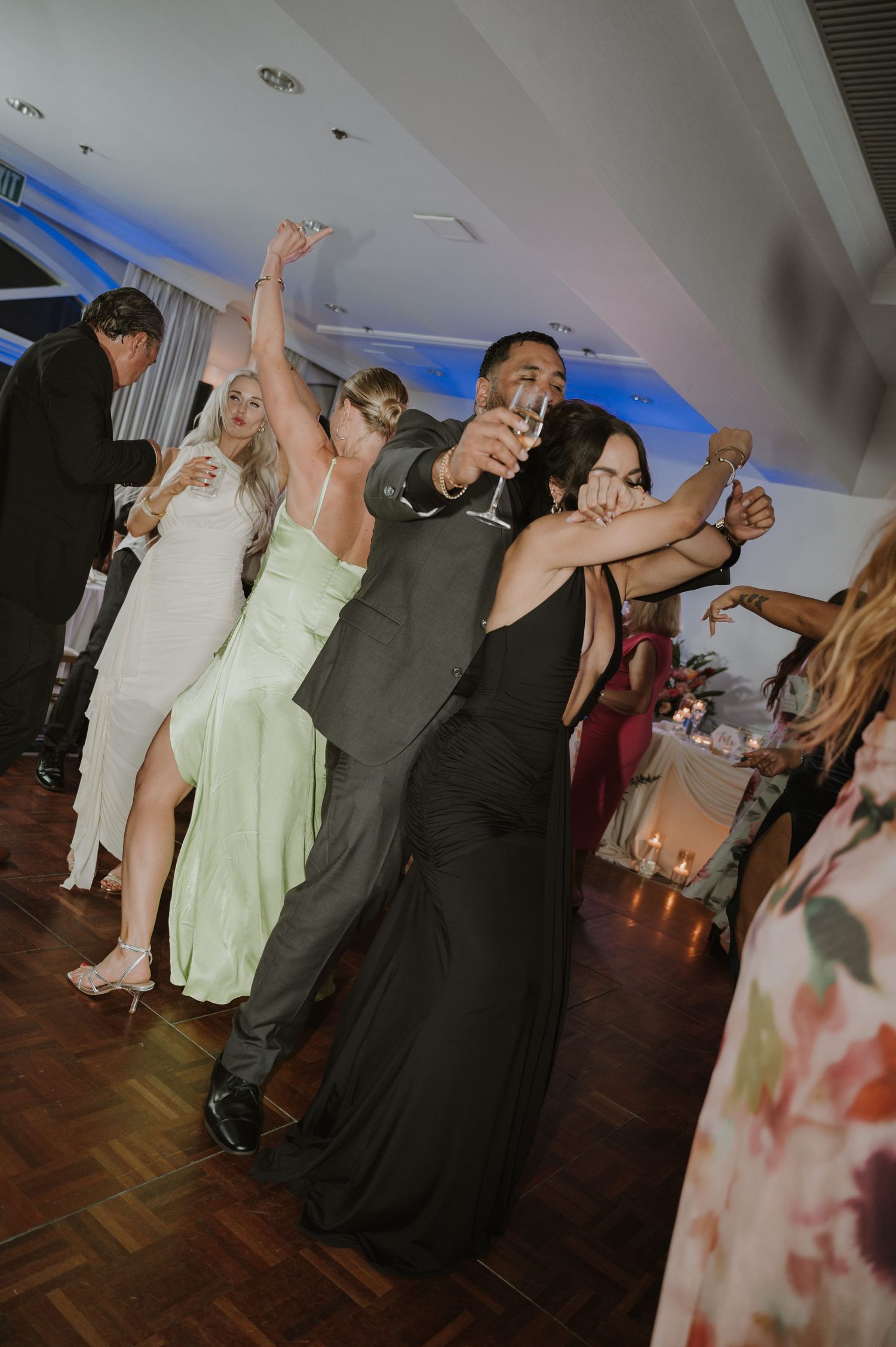 Wedding guests dancing with raised arms on a wooden dance floor during evening celebration.