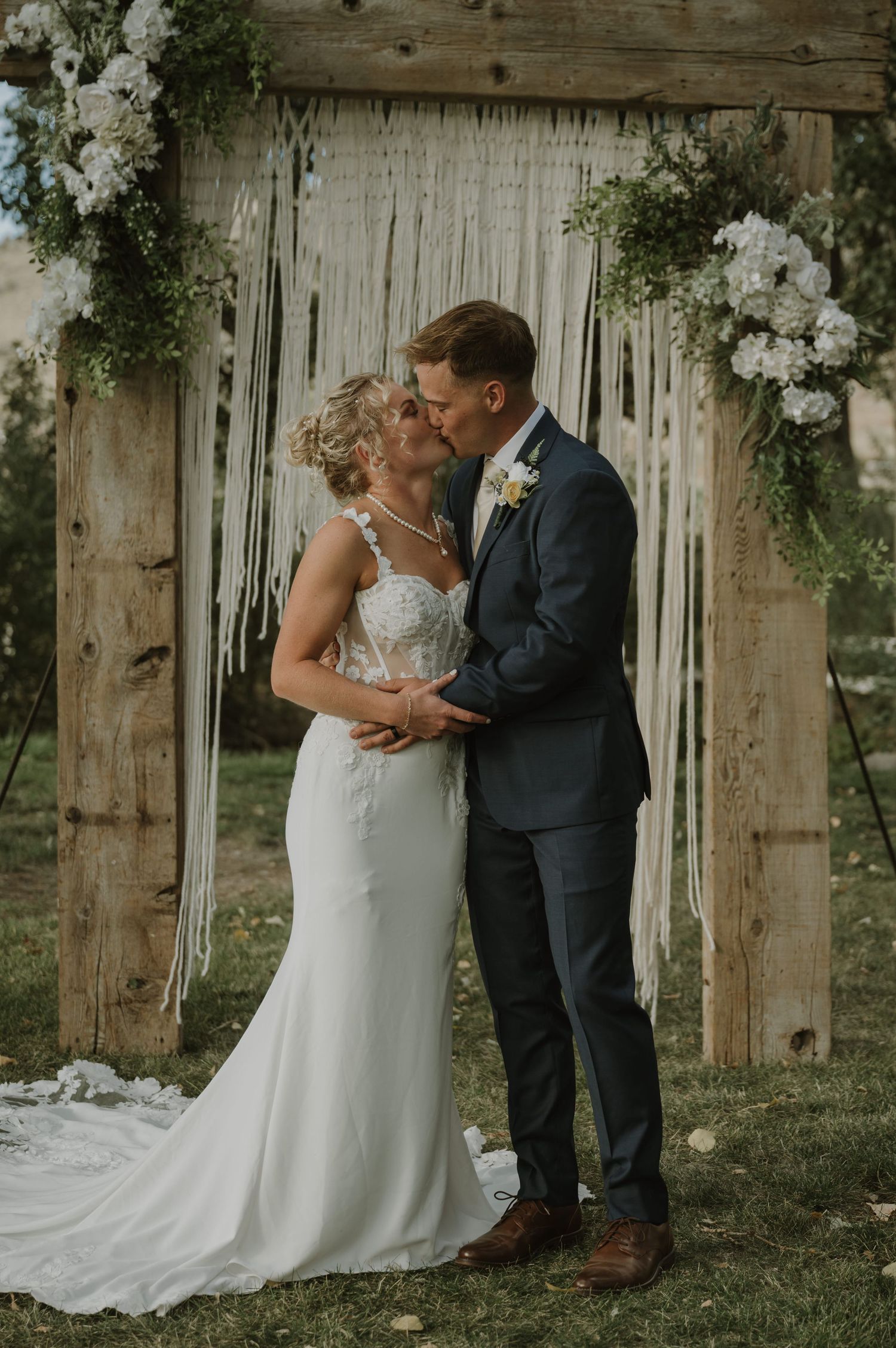 A romantic wedding moment captured in front of a macrame backdrop with white floral arrangements.