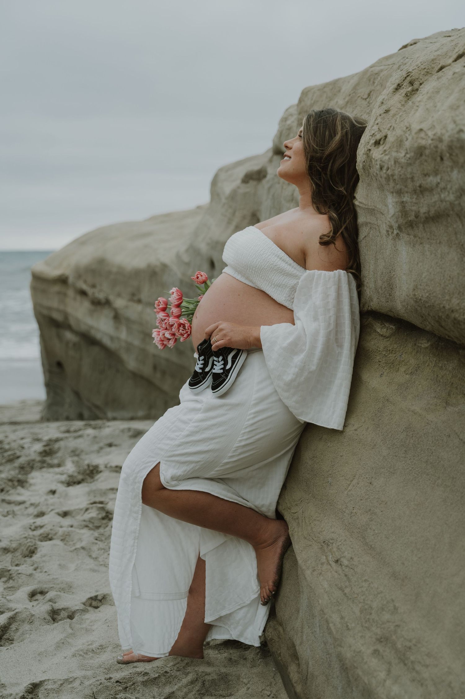 Intimate maternity photos captured against coastal rock formations at sunset.