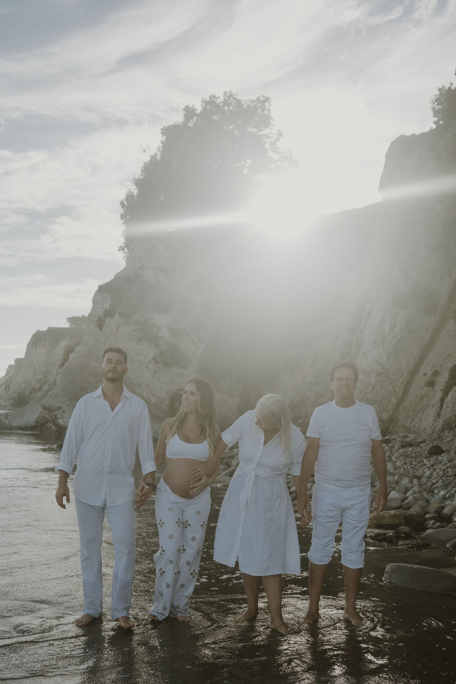 A group poses together on a rocky beach at sunset with cliffs behind them.