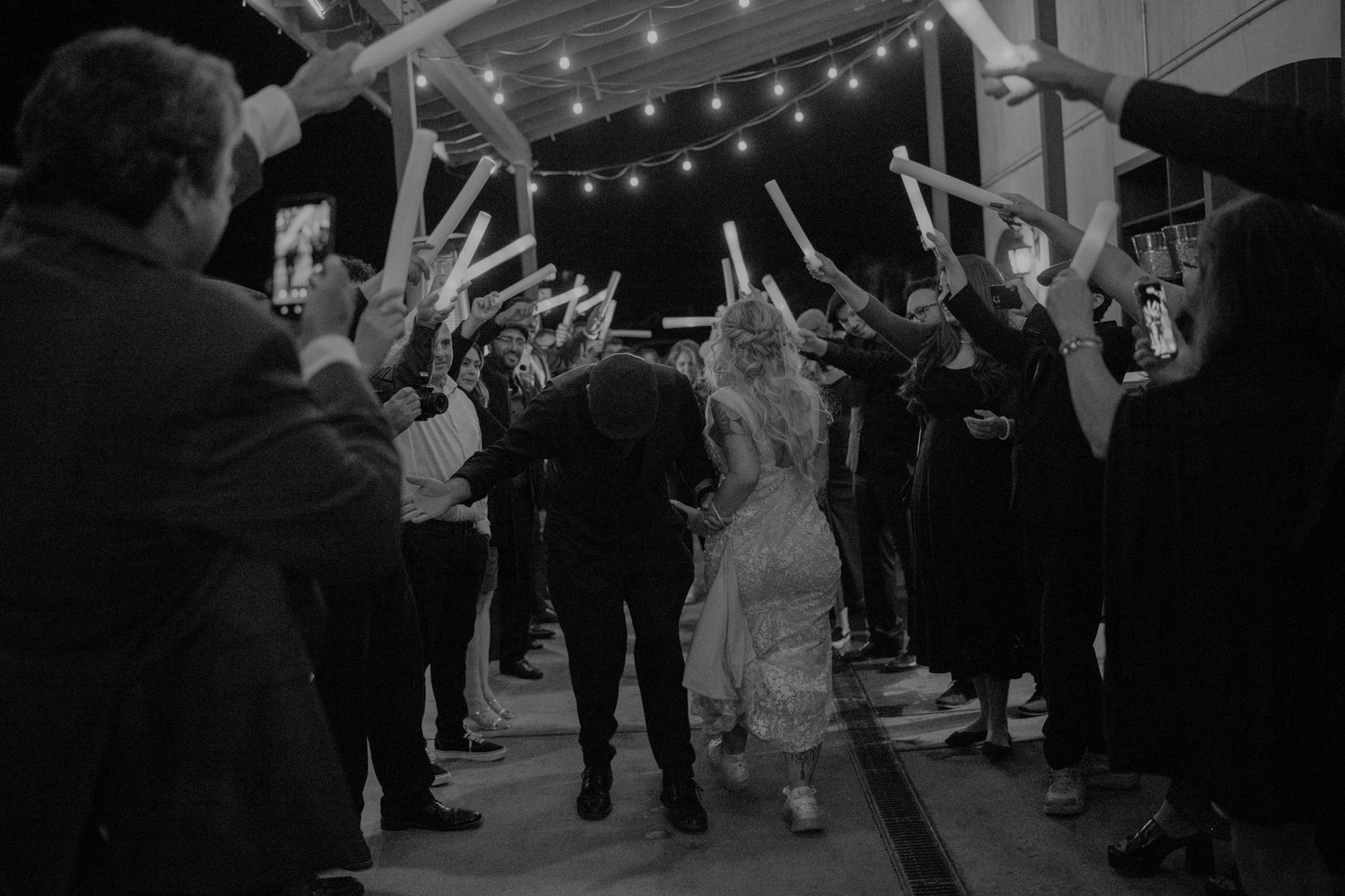 Wedding guests form a sparkler tunnel for the newlyweds under twinkling string lights.