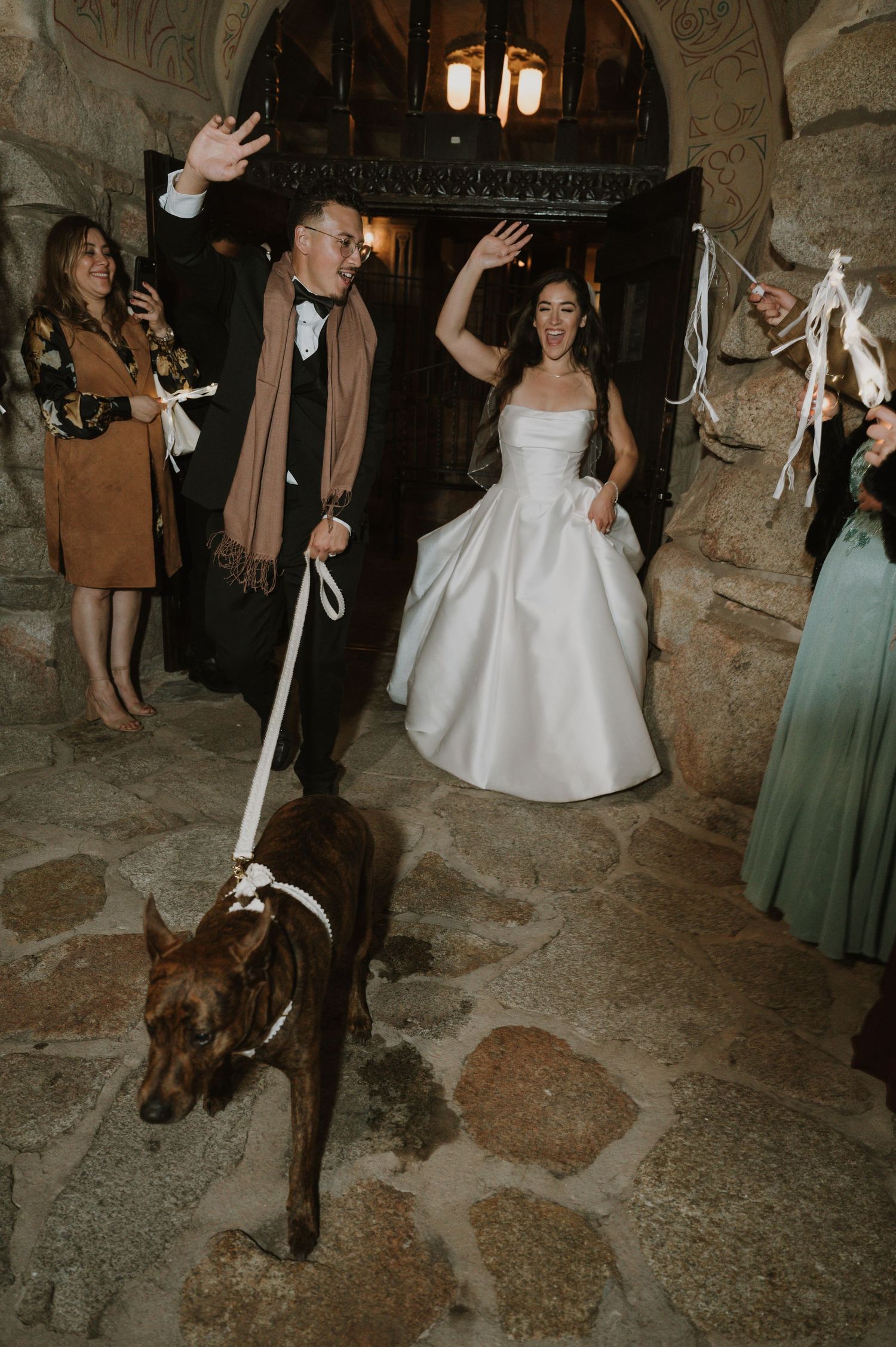Wedding guests dance and celebrate in an elegant stone-walled venue with mood lighting.