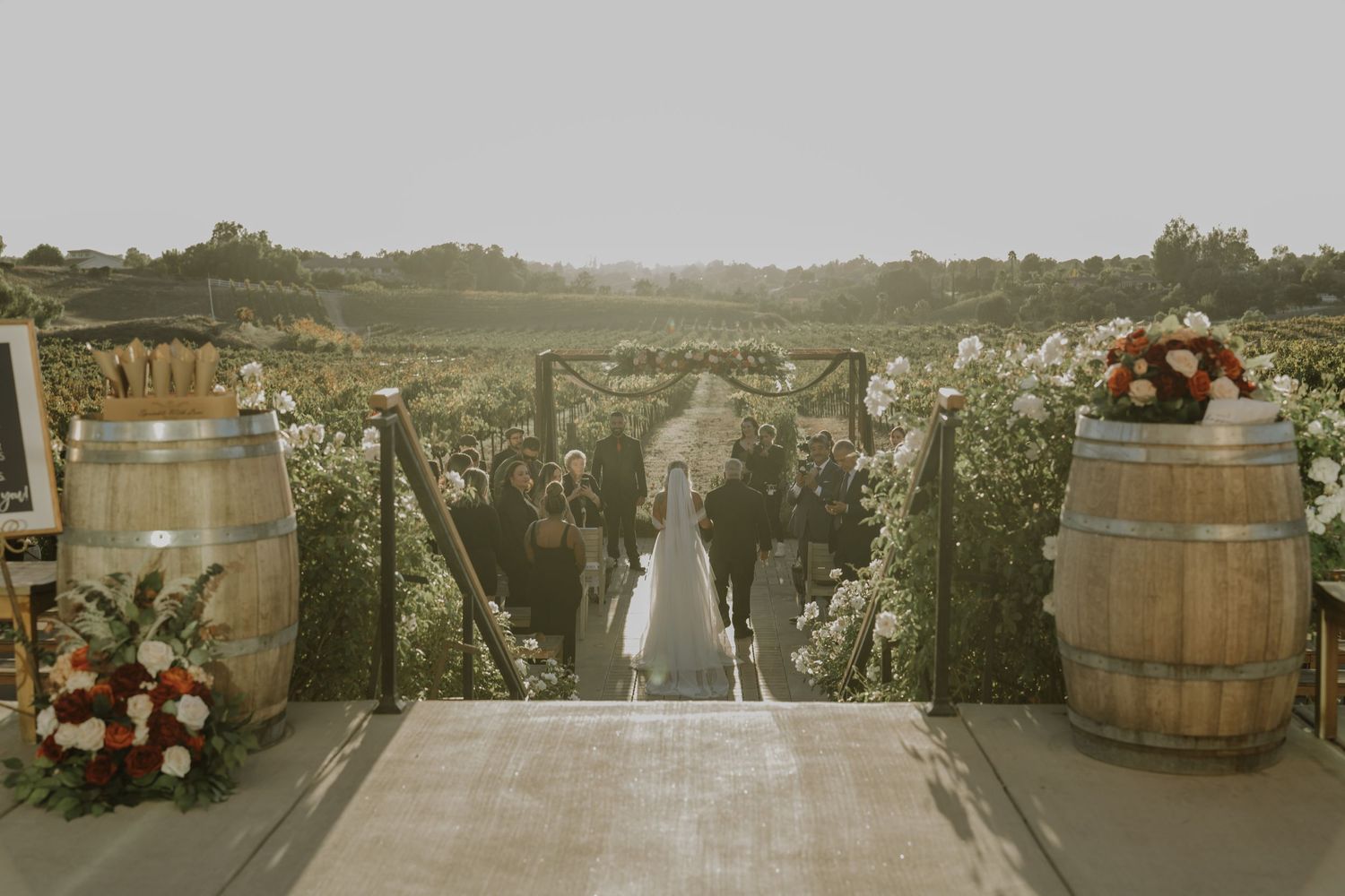 Wedding ceremony setup with wine barrels and floral arrangements overlooking vineyard.