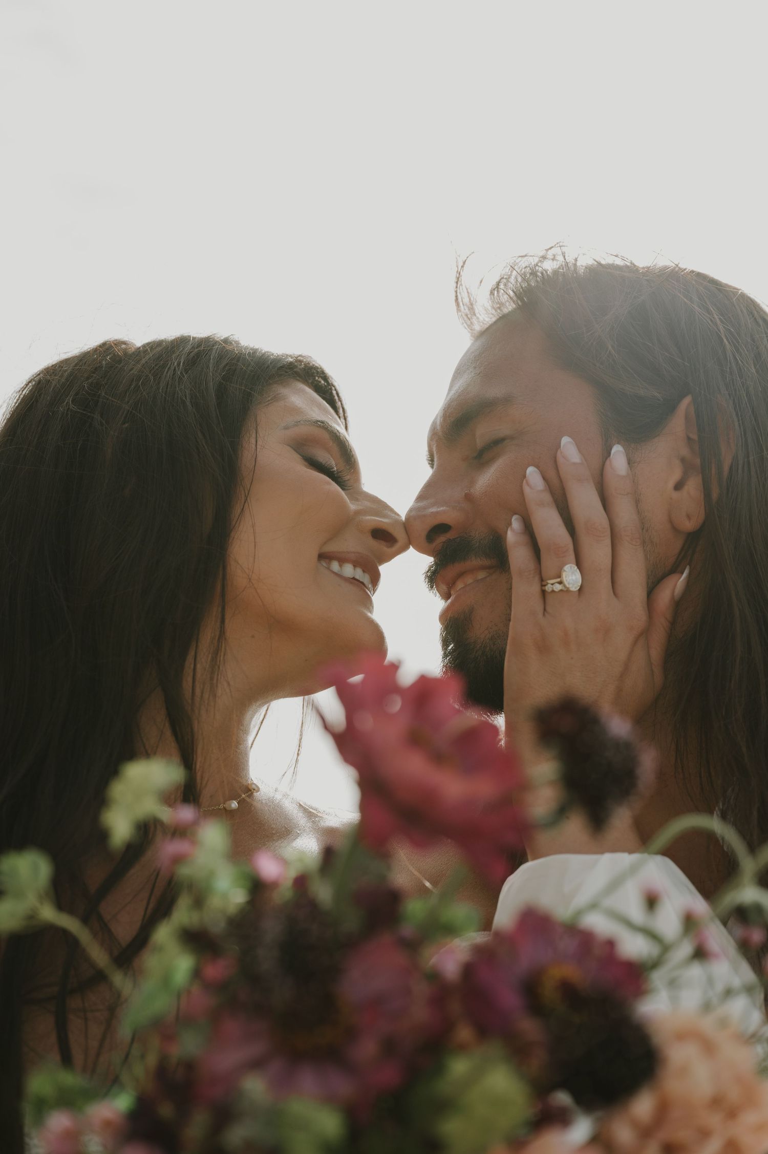 An intimate close-up of a couple kissing with pink flowers in the foreground.