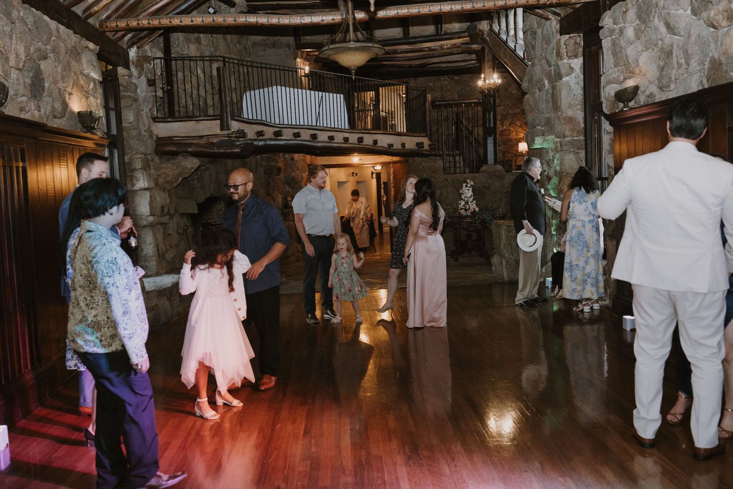 Guests dancing and mingling inside a rustic stone venue with warm wood floors during a wedding reception.