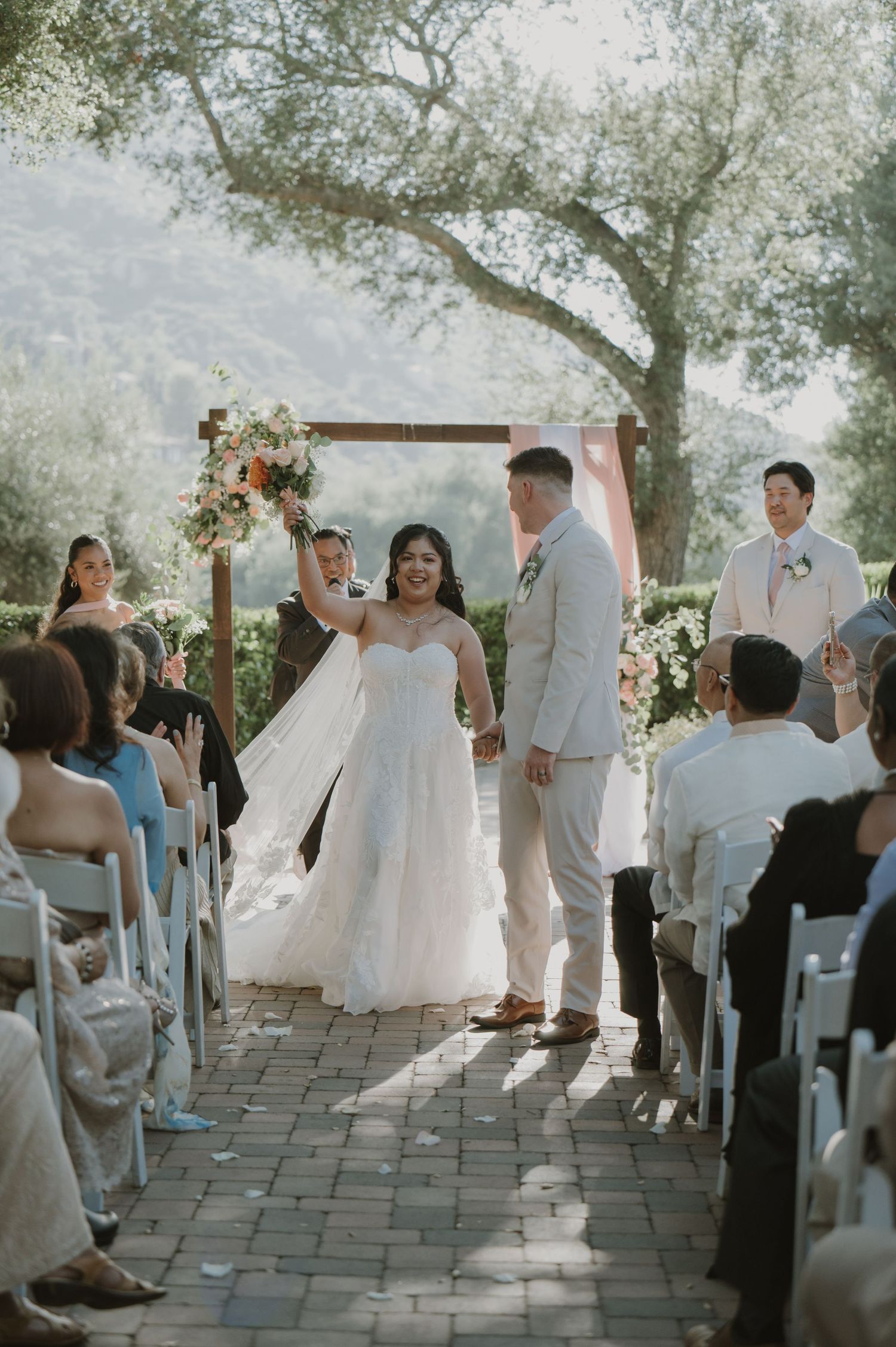 Bride and groom celebrate at outdoor wedding ceremony altar surrounded by guests and floral arch.