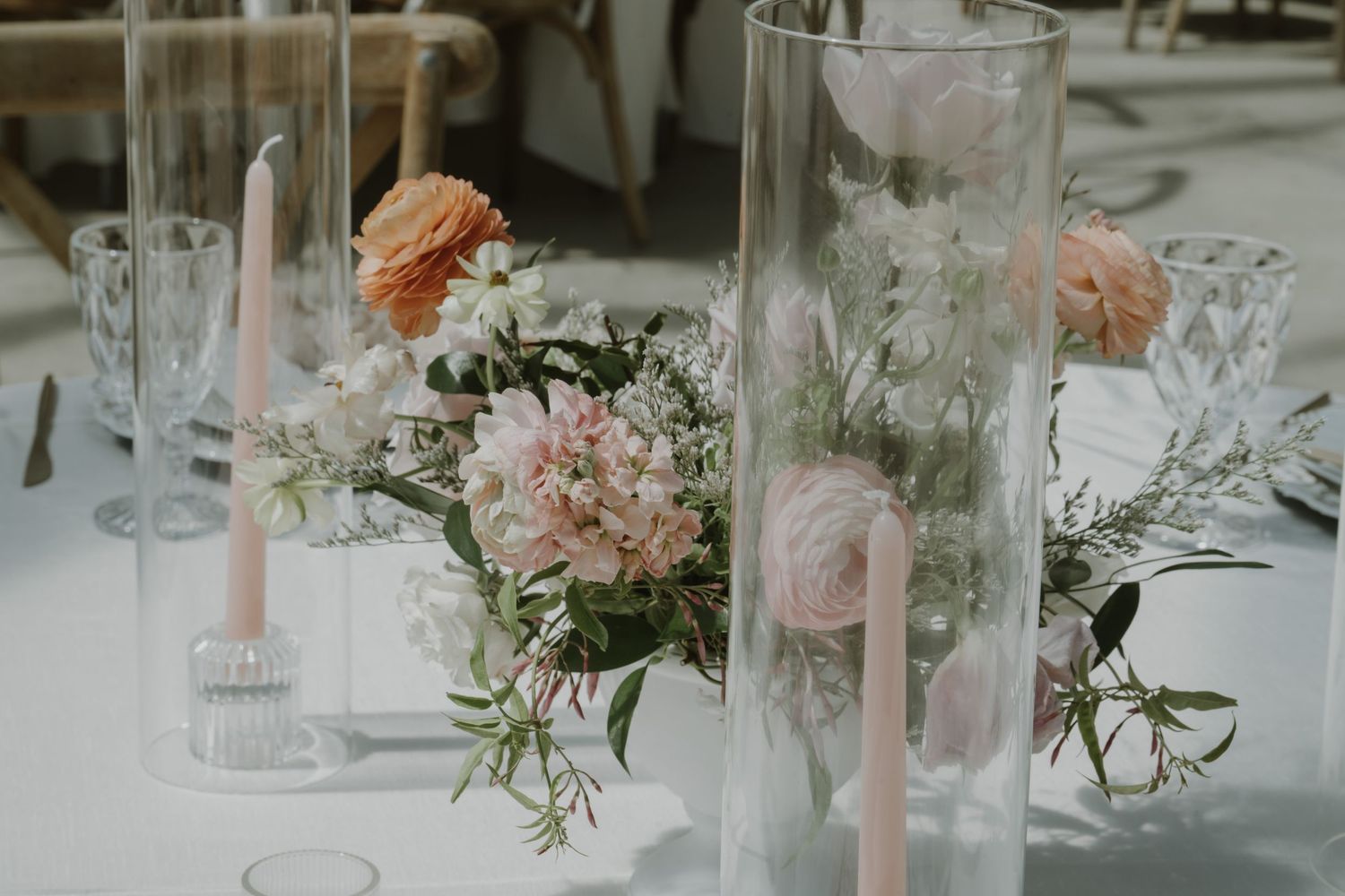 Elegant wedding table centerpiece with blush pink roses, ranunculus, and tapered candles in glass holders.