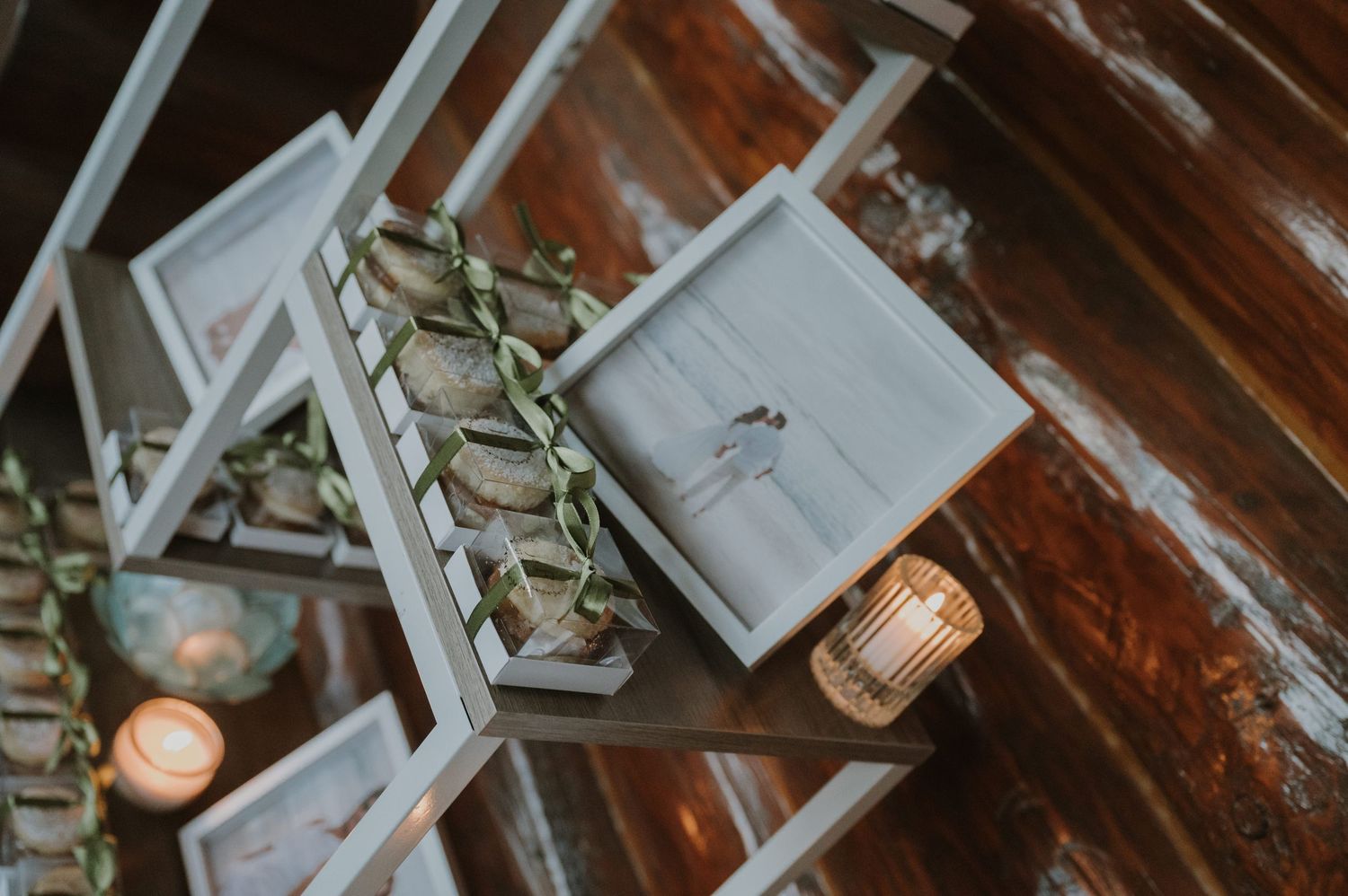 Rustic wooden wall display with gray framed photos, greenery accents, and glowing candles at a wedding reception.