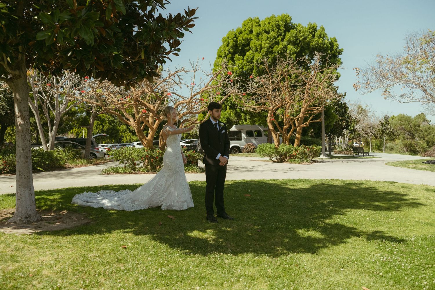 Bride and groom share a first look moment on lush green lawn surrounded by trees at an outdoor wedding venue.