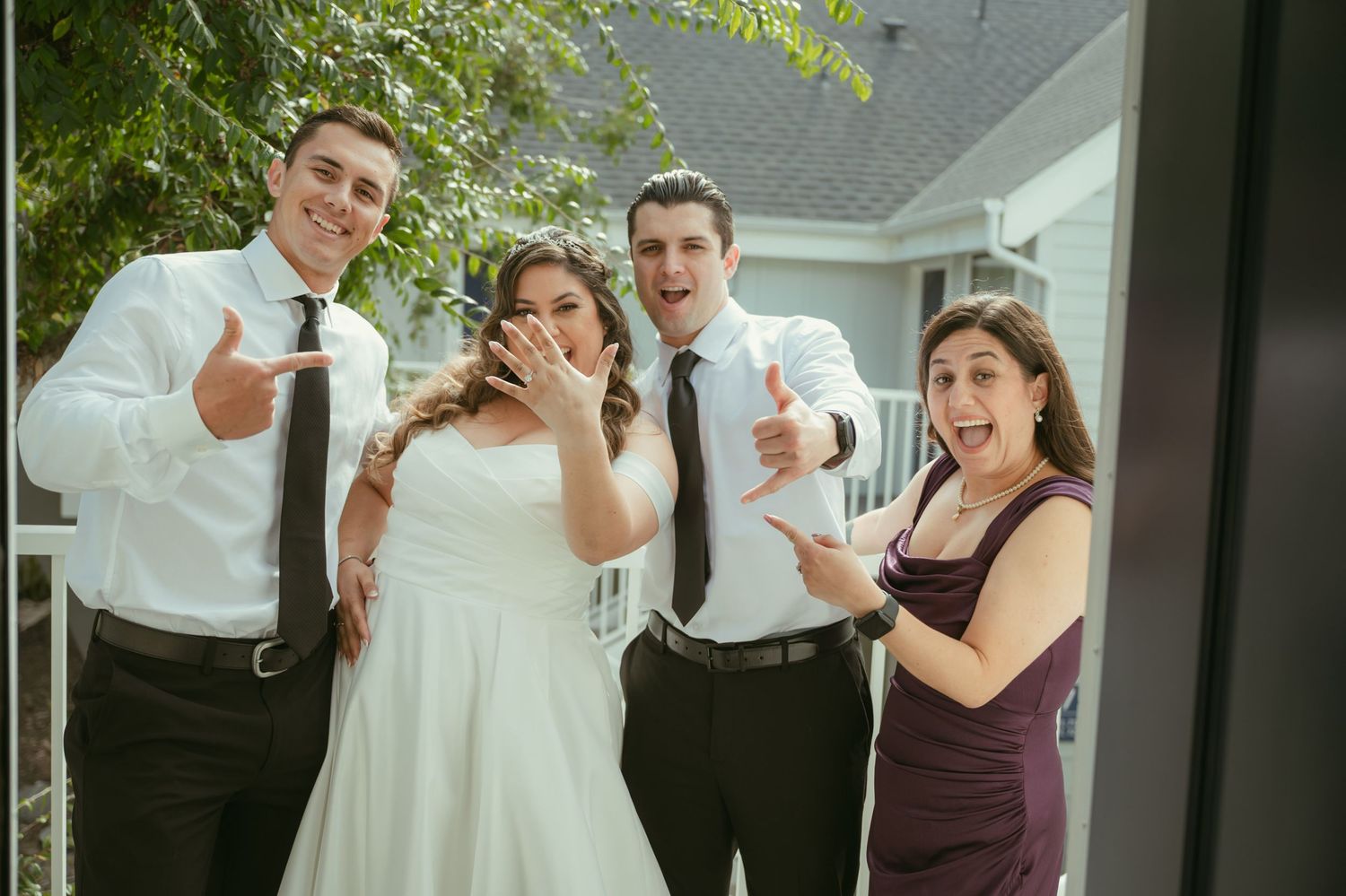 Bride in white dress poses with groom and guests giving thumbs up at outdoor wedding celebration.