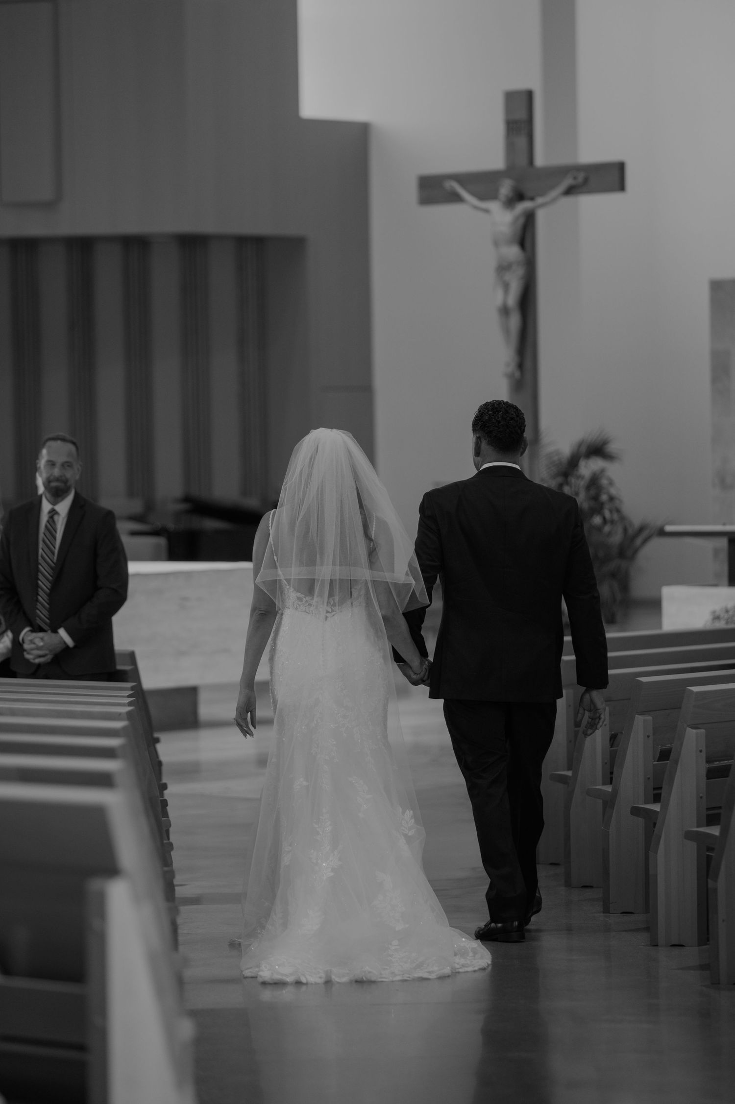 Black and white photo of a bride and groom walking hand in hand down the aisle of a Catholic church.