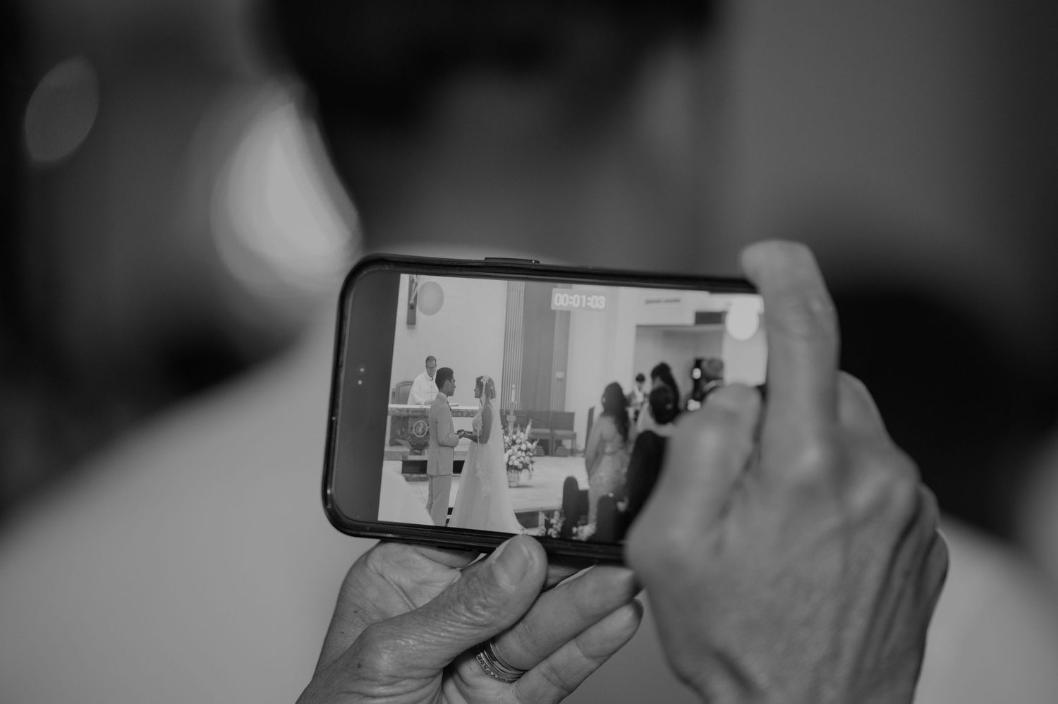 Guest captures wedding ceremony on smartphone in black and white photo.