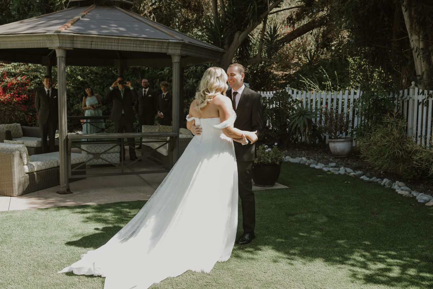 Bride and groom share a romantic dance on green lawn with garden gazebo backdrop on their wedding day.