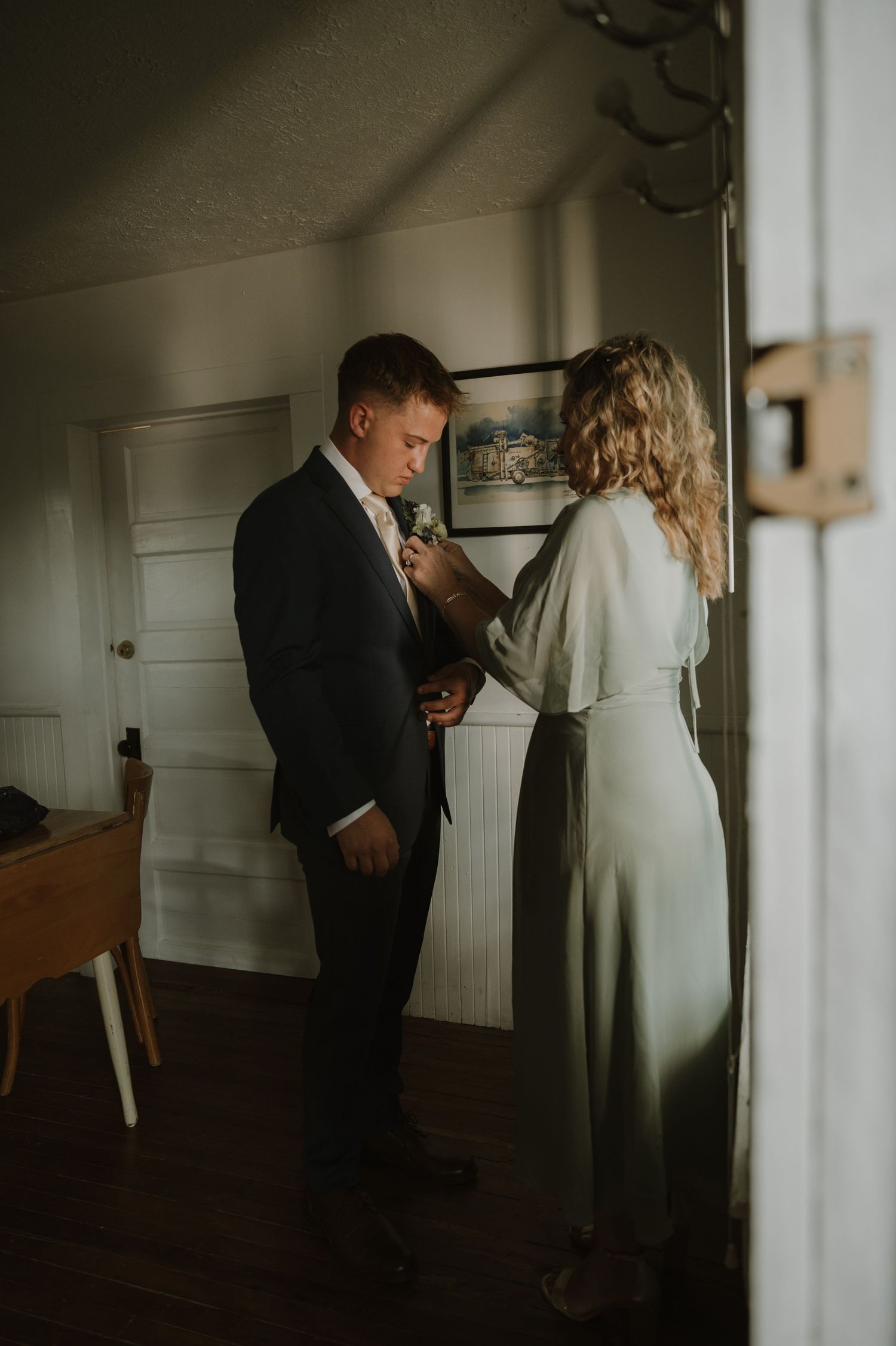 A couple embraces in a softly lit room with white walls and natural window light.