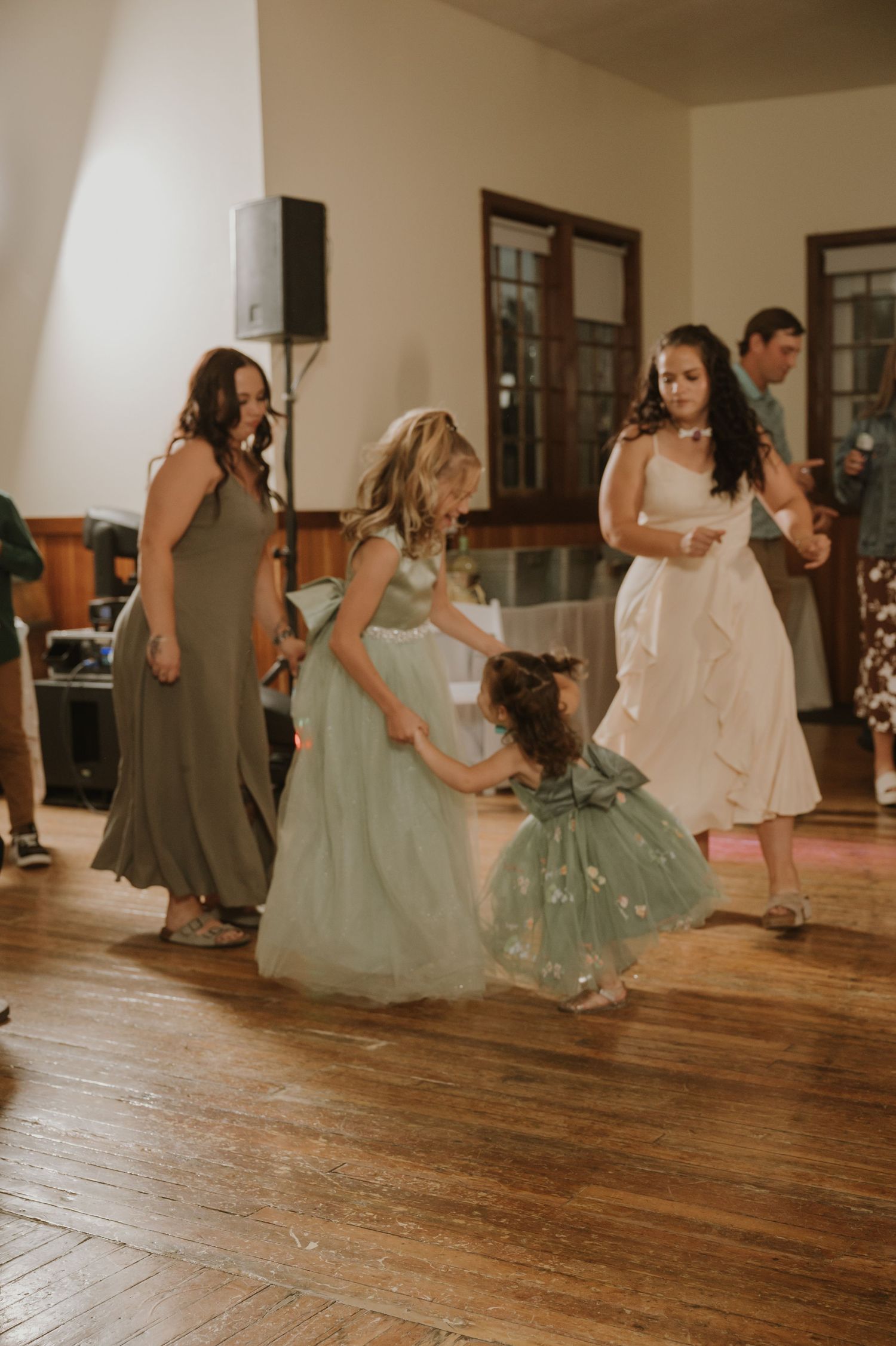 Wedding guests in formal attire dancing on a rustic wooden floor.