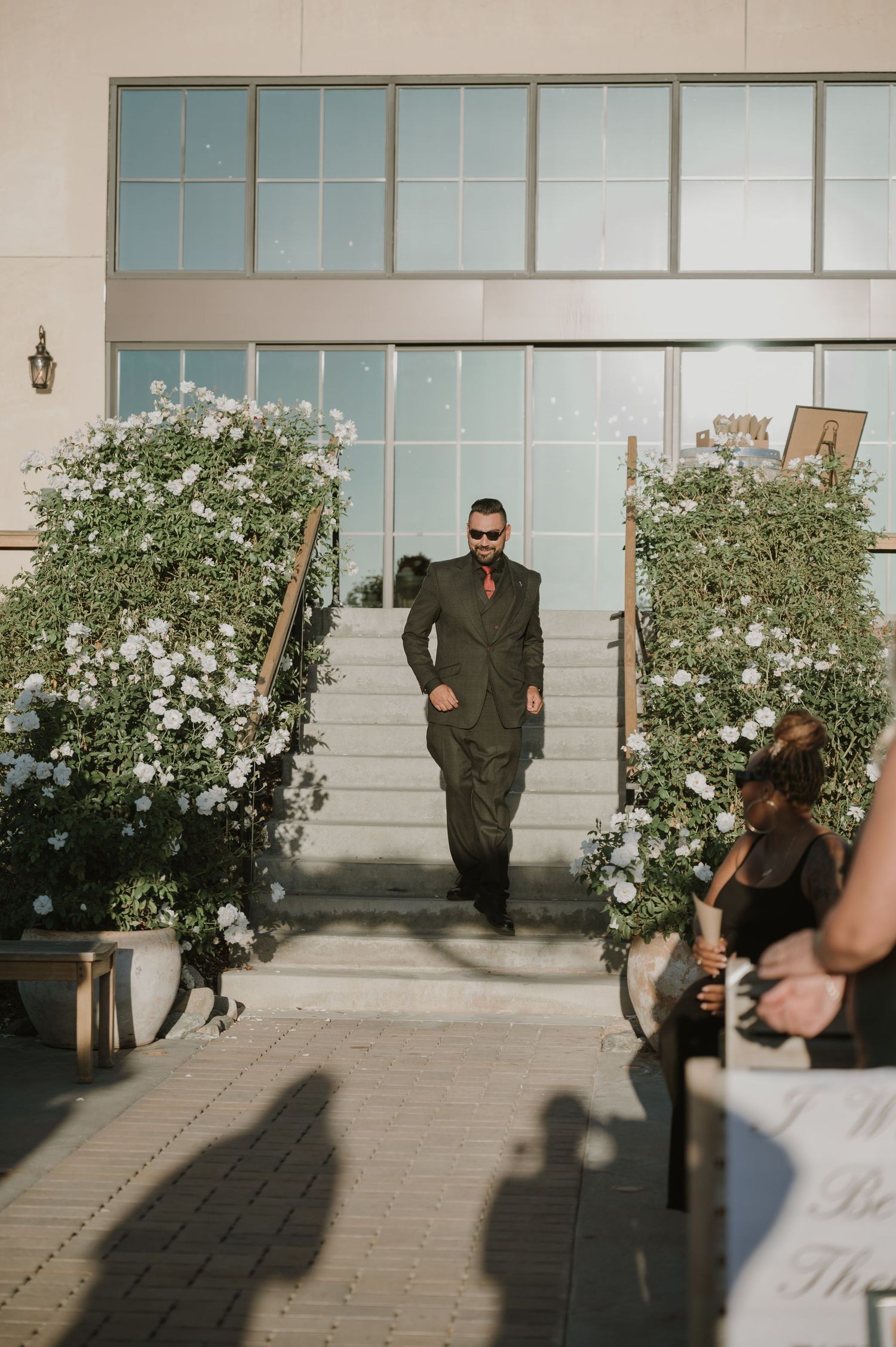 Wedding ceremony setup with white floral arches and modern glass building backdrop.