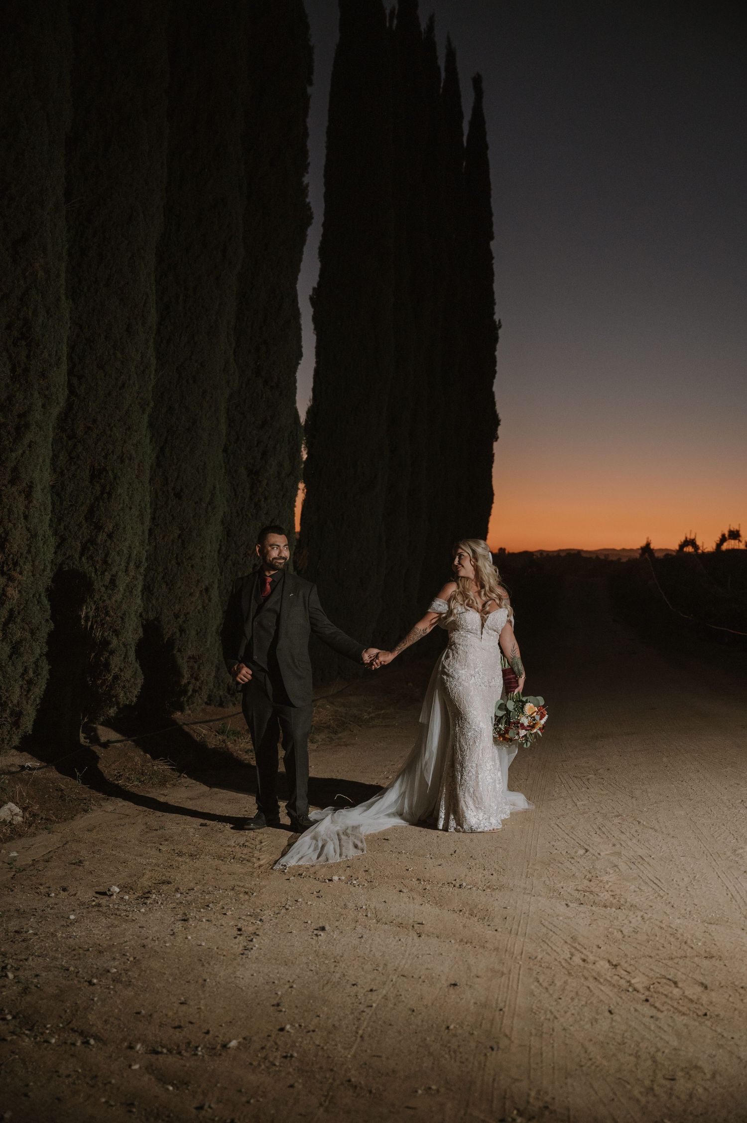 Dramatic nighttime wedding portraits with tall cypress trees and sunset backdrop.