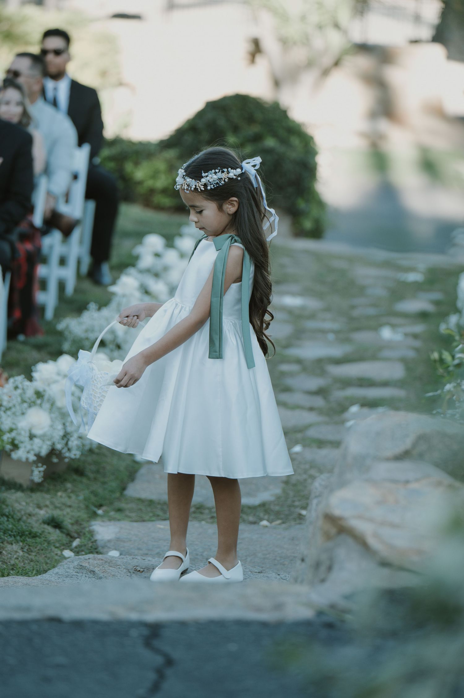 Young flower girl in white dress walking along garden path.