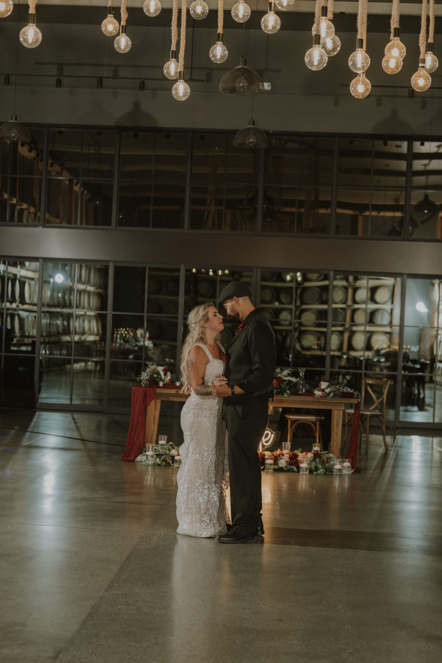 A couple shares their first dance in an industrial venue with hanging Edison bulbs creating a romantic atmosphere.