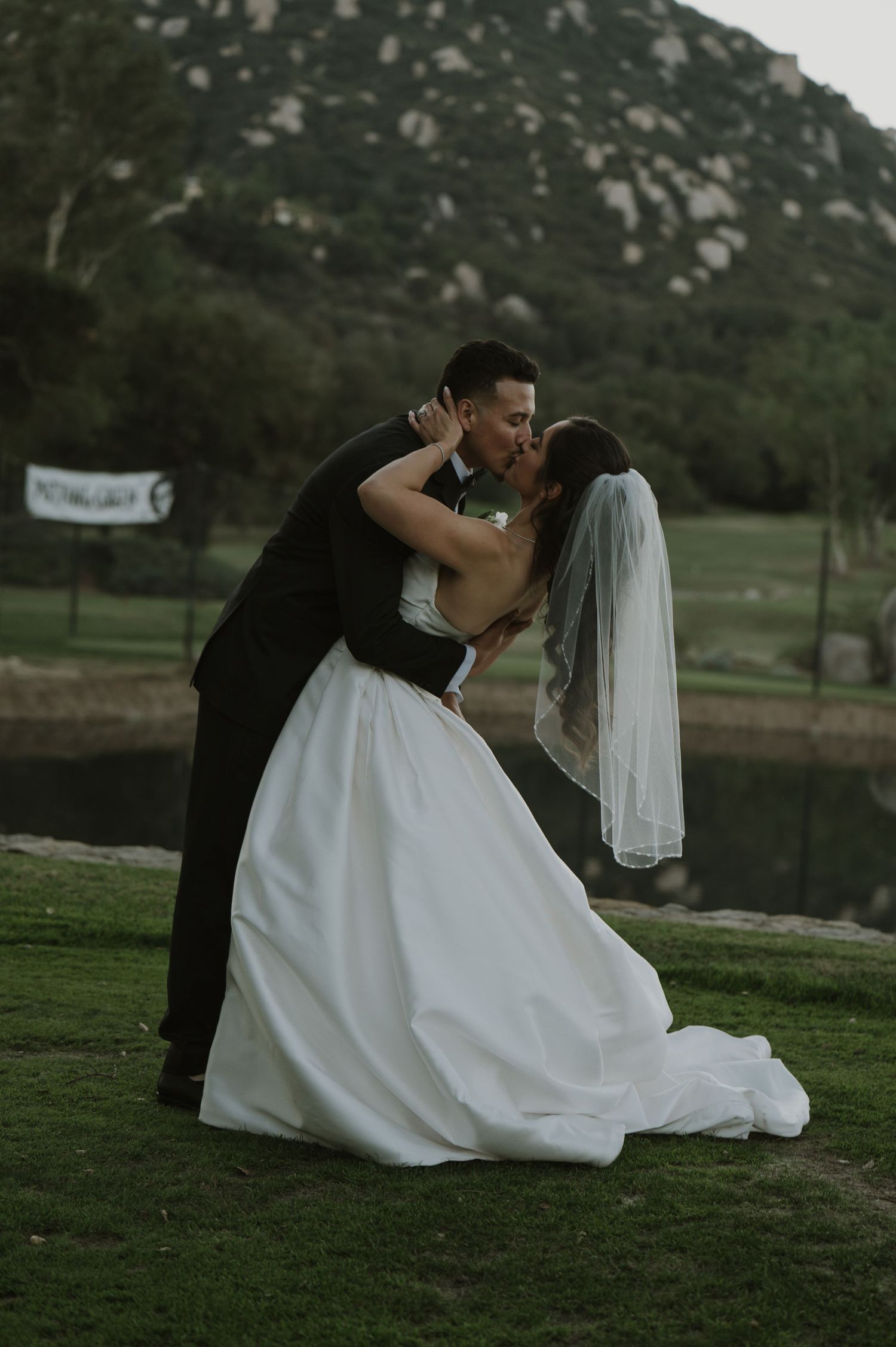 Romantic wedding dip pose with bride in flowing white dress against mountain backdrop.