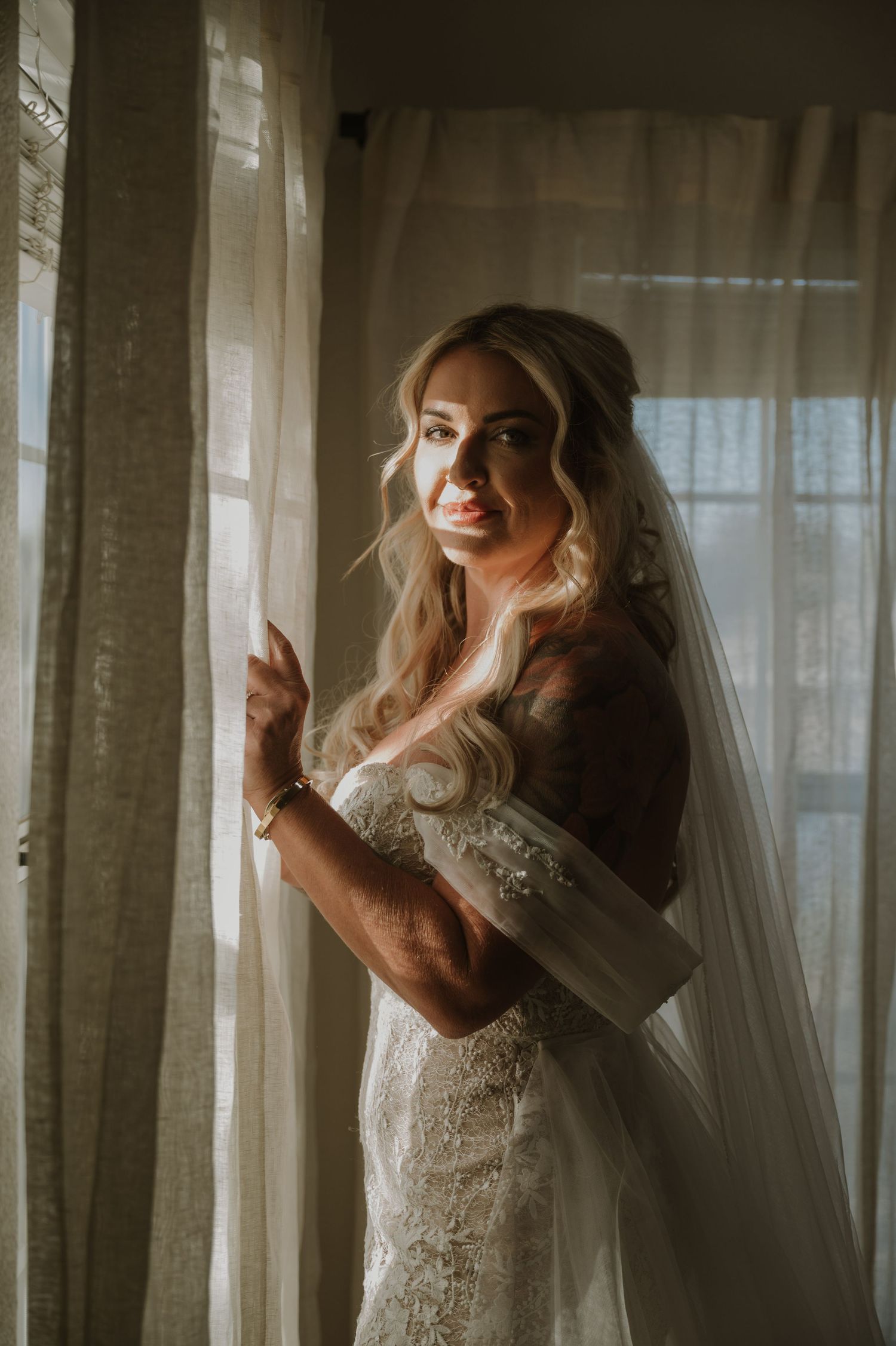 Ethereal bridal portrait with sunlight streaming through sheer curtains creating a dreamy atmosphere.