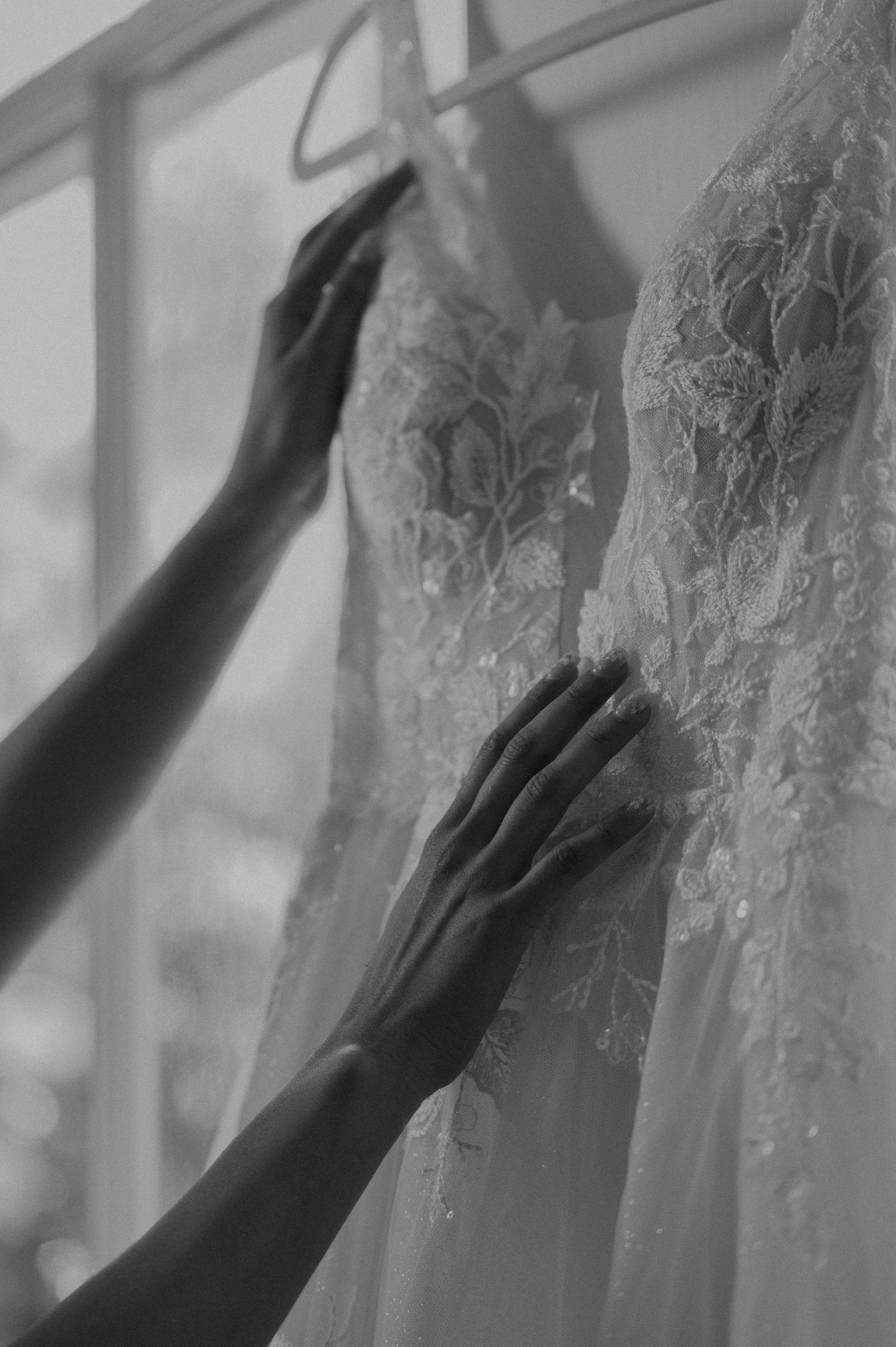 Black and white close-up of bride's hands gently touching intricate lace details of her wedding dress.