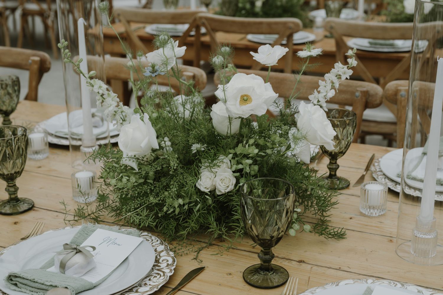 Elegant wedding table centerpiece with white roses, poppies, and lush greenery on a rustic wood farm table.