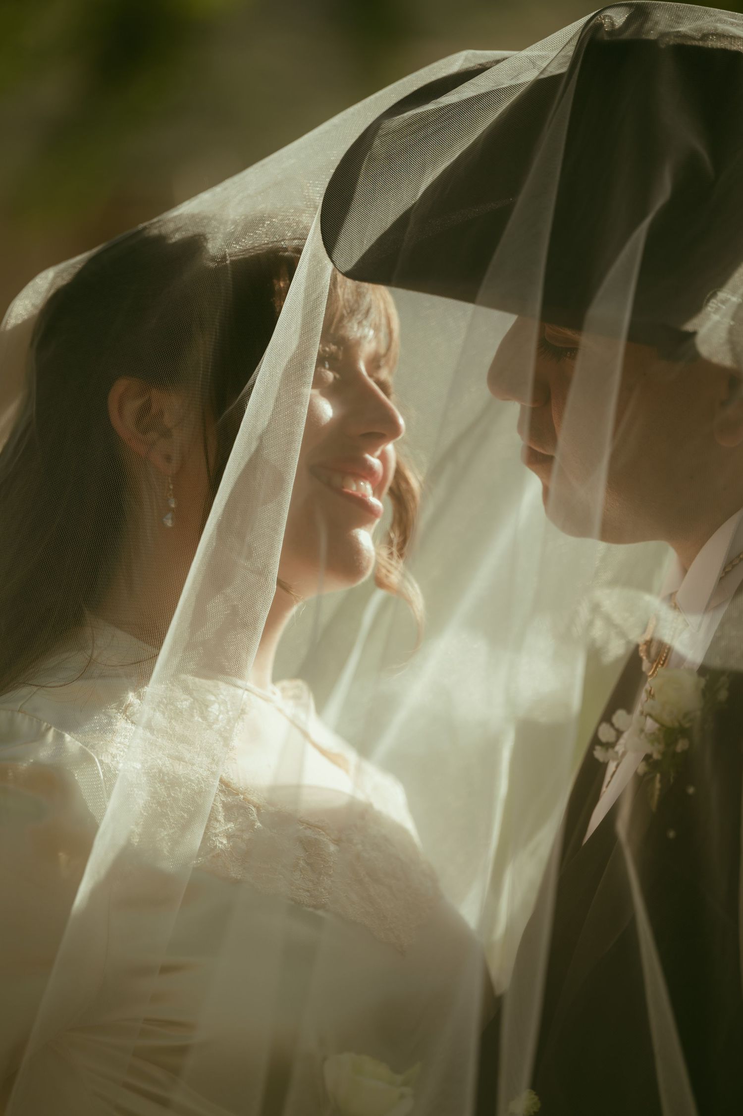 Bride and groom share an intimate moment under a flowing white veil, bathed in soft golden light.