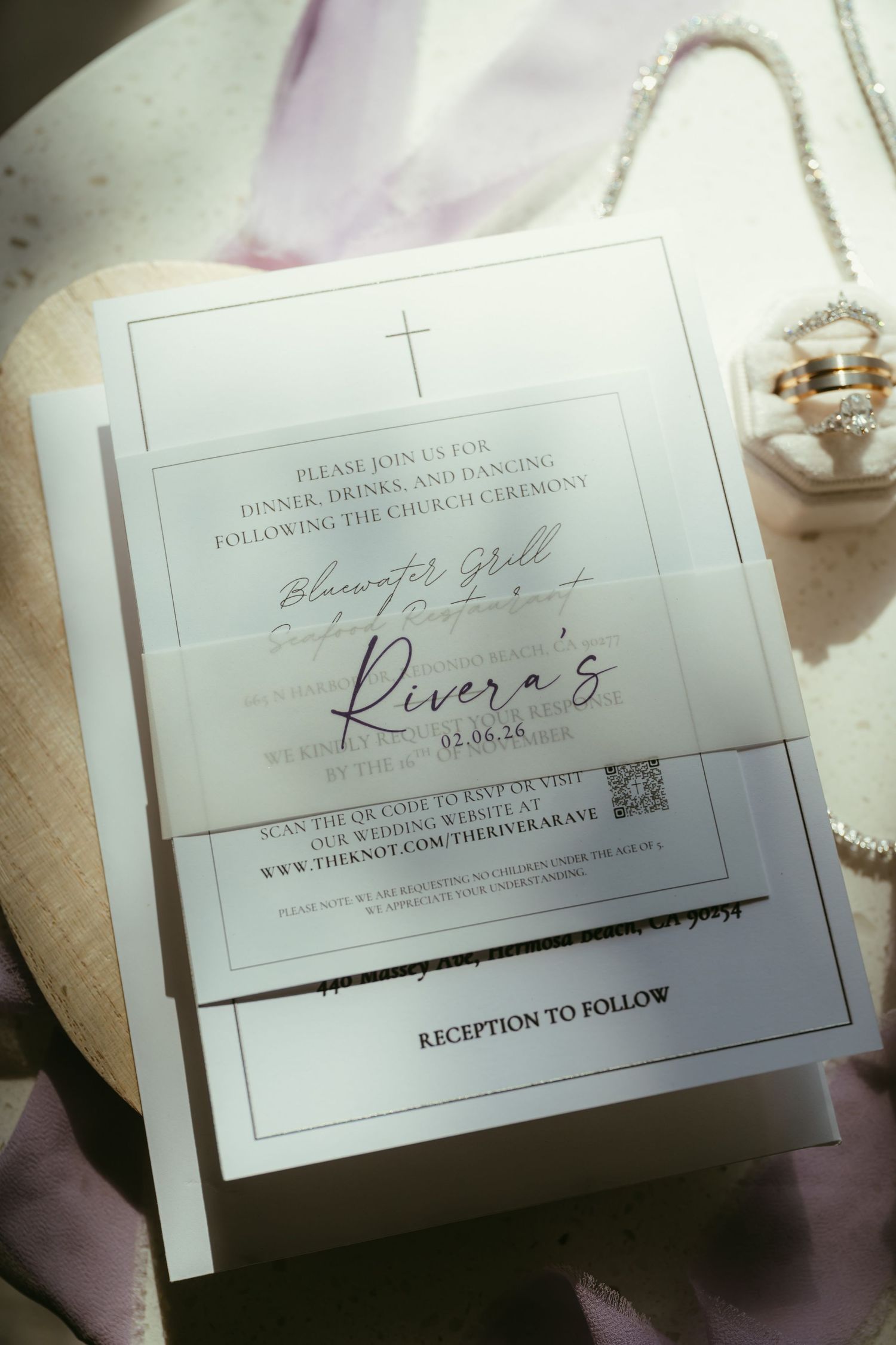 Elegant wedding reception invitation for the Riveras with a cross, vellum overlay, and QR code, styled with jewelry accents.