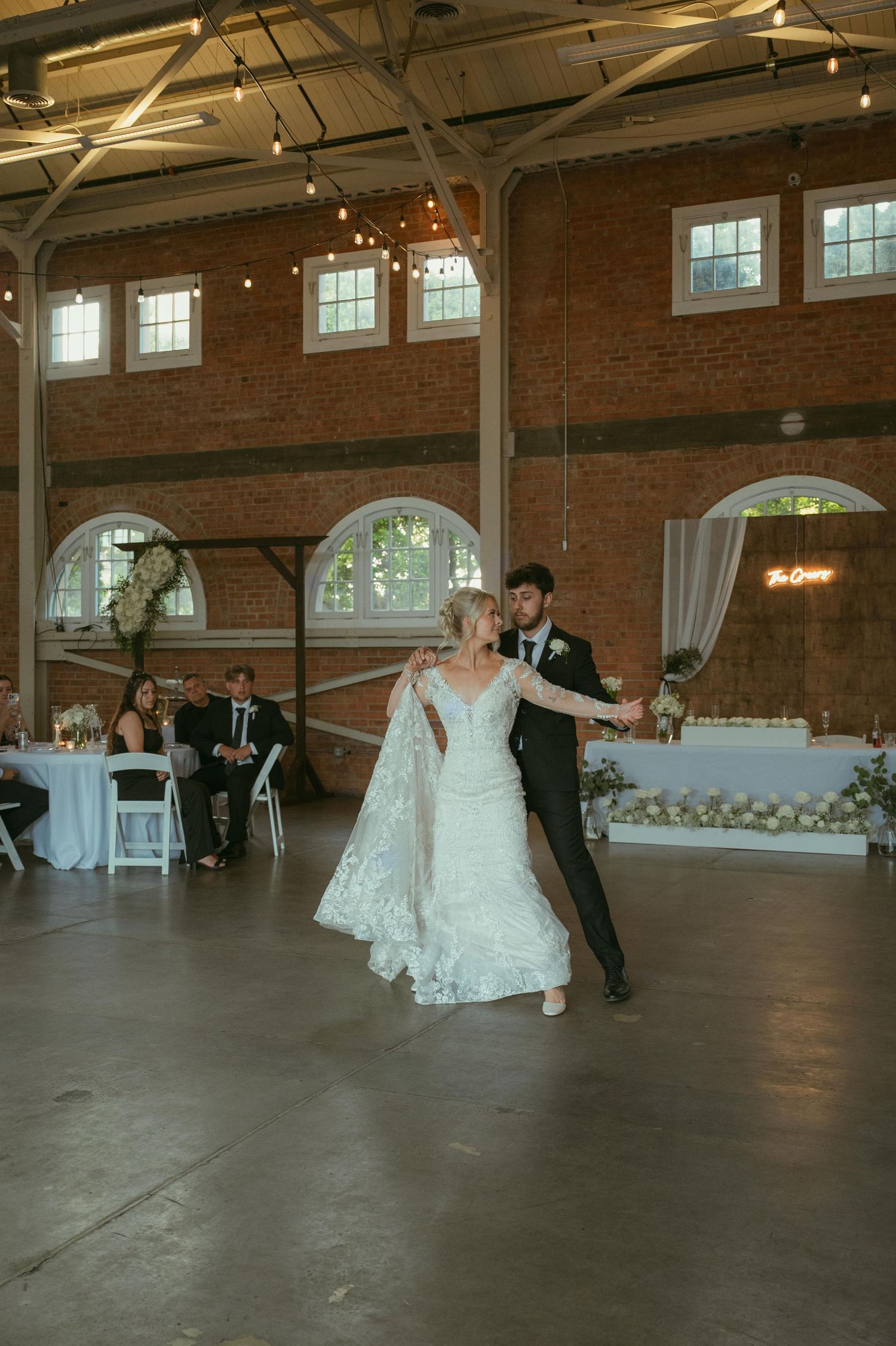 Bride and groom share their first dance in a stunning industrial brick venue with string lights overhead.