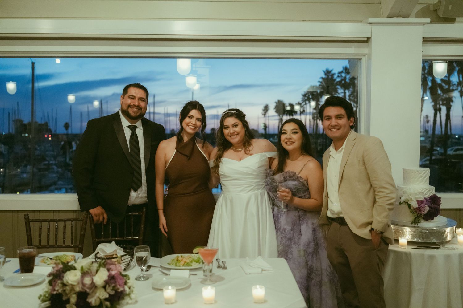 Wedding party poses together at elegant waterfront venue during evening reception with harbor views.