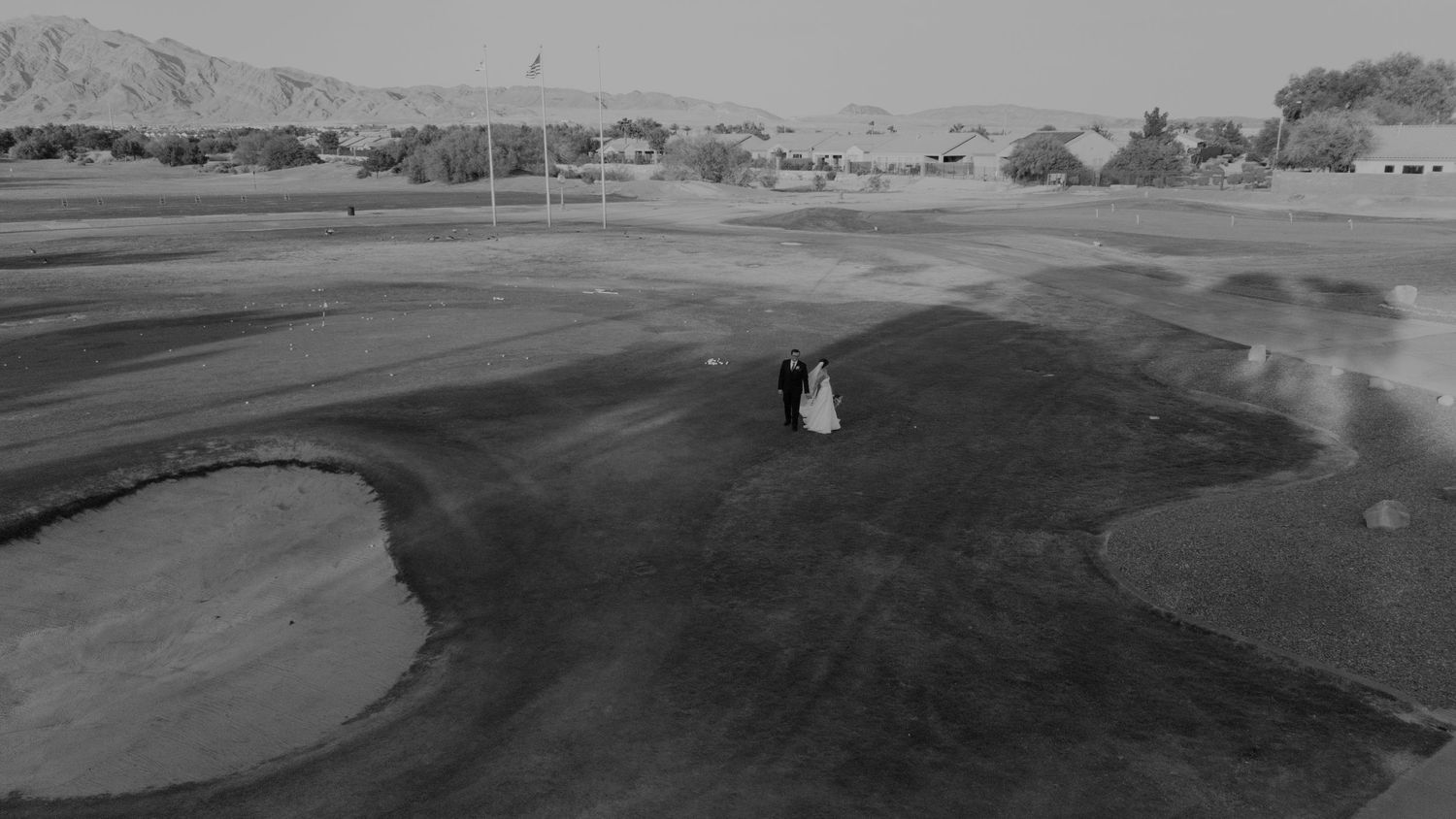 Black and white aerial drone photo of a bride and groom standing together on a golf course landscape.