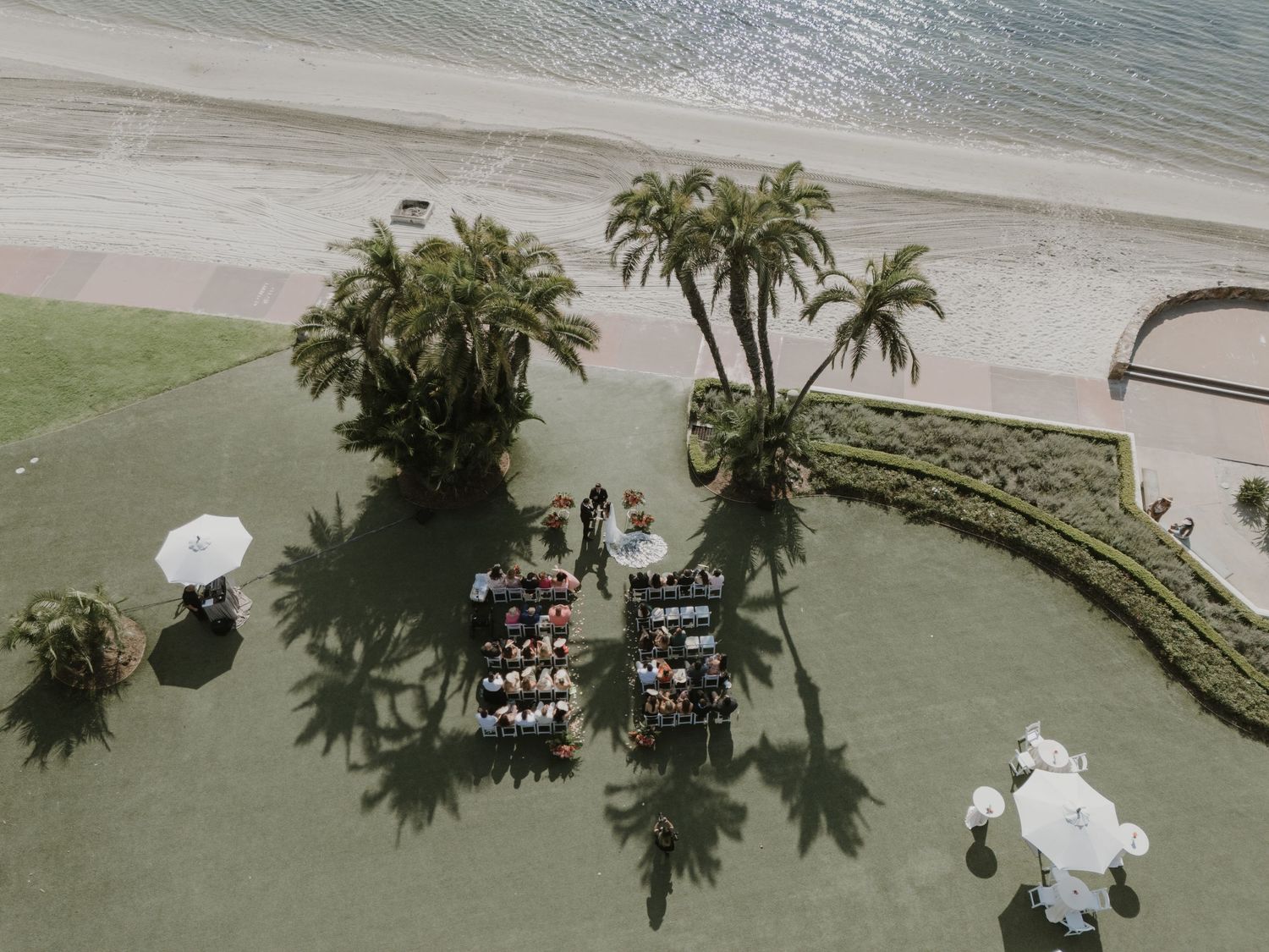 Aerial view of a waterfront wedding venue with white chairs and palm trees.