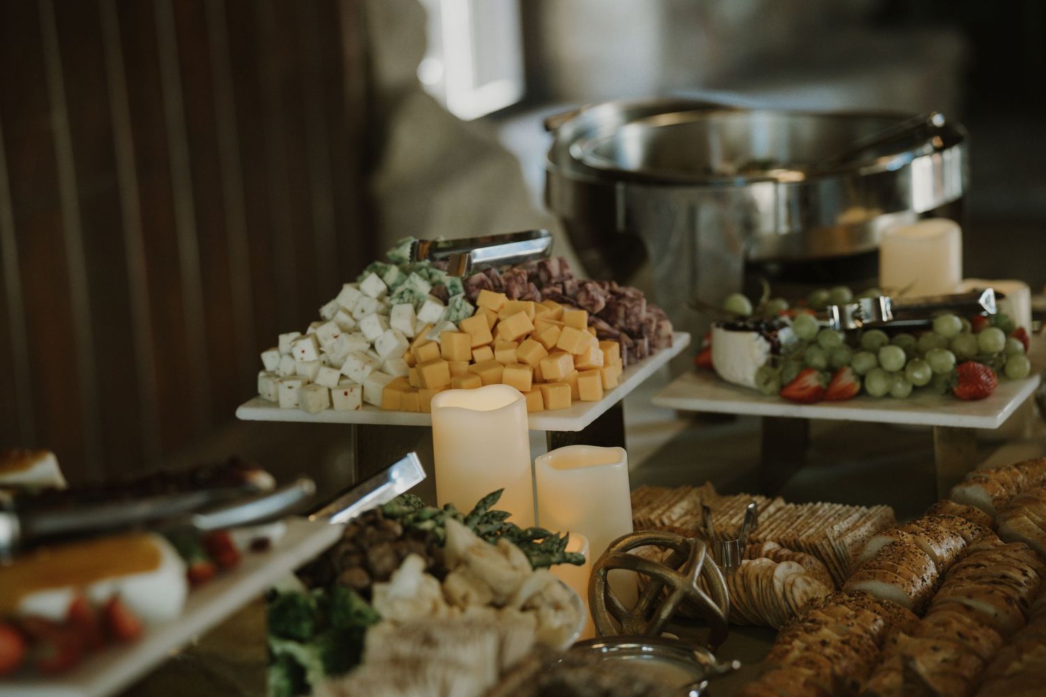 An elegant wedding reception buffet table with cheese, fruit, and candles.