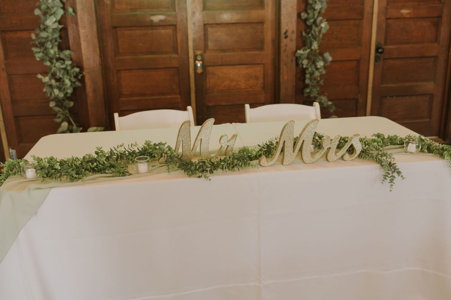 Wedding reception table decorated with fresh greenery garlands and white linens.