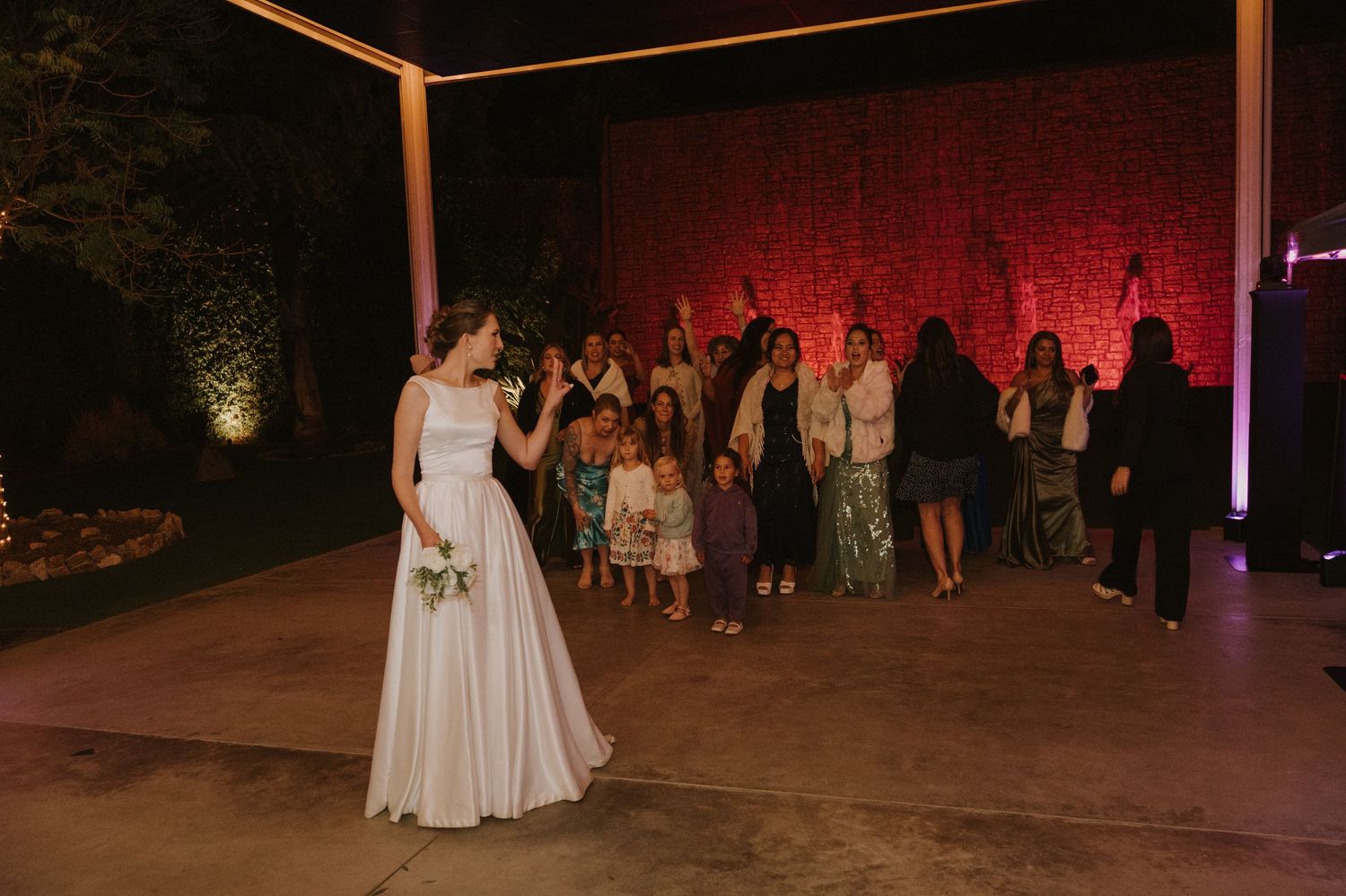 Bride in white gown prepares to toss bouquet to guests at outdoor wedding reception.