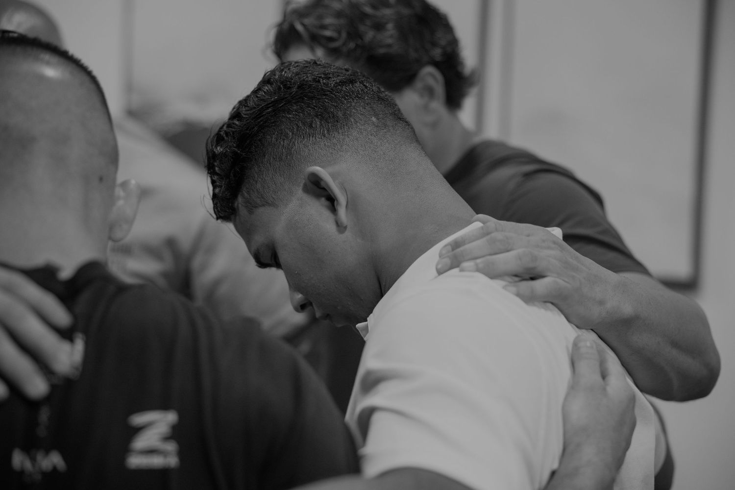 Black and white photo of groomsmen sharing an emotional group hug before a wedding ceremony.