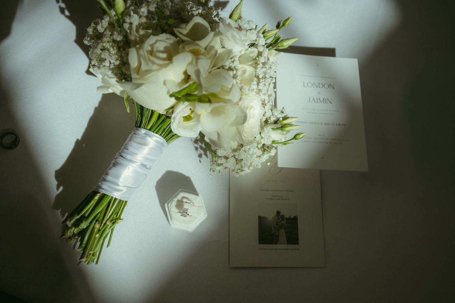 White wedding bouquet with roses beside elegant invitation cards on a light surface with soft shadows.