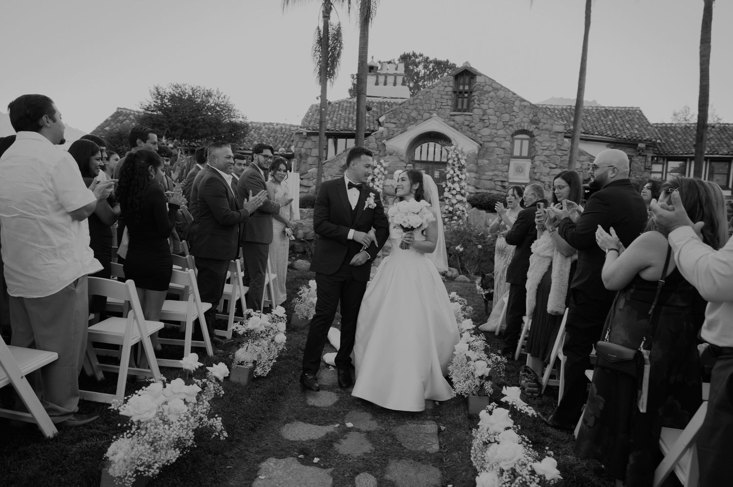 A wedding recessional along a stone path with guests standing and applauding.