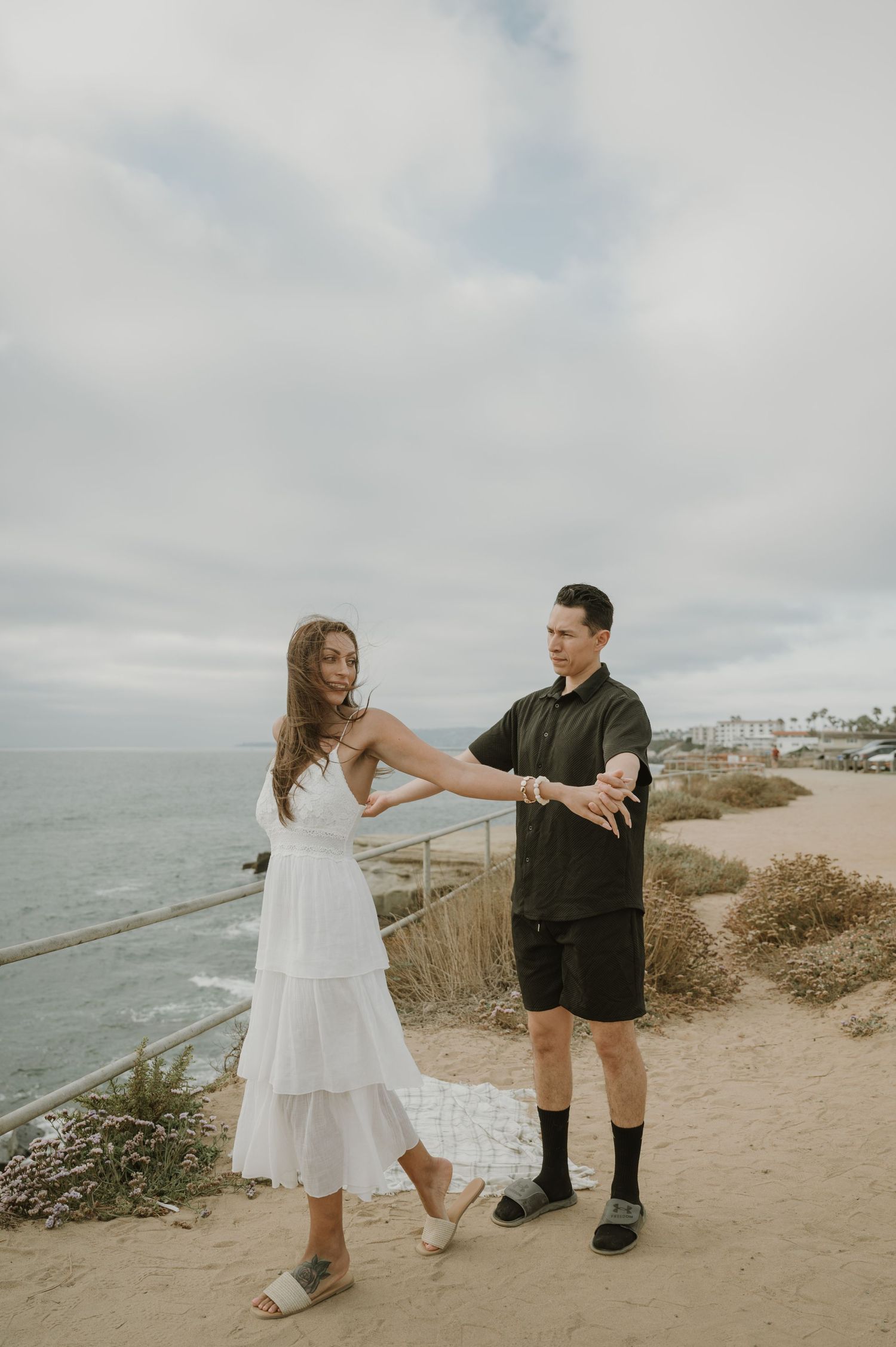 Couple dancing and twirling on coastal path with ocean views.