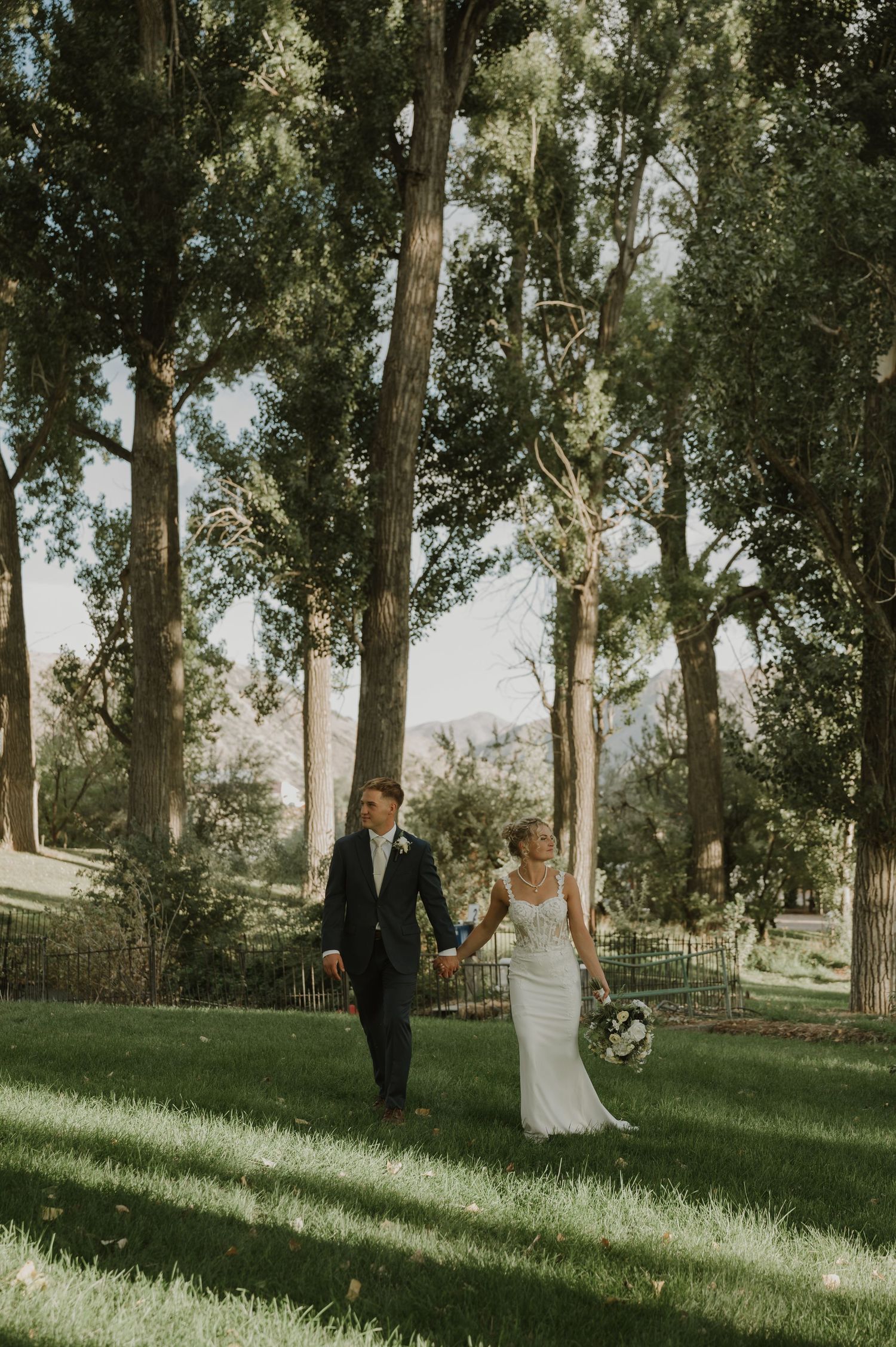 A couple walks through a scenic grove of tall trees on their wedding day.
