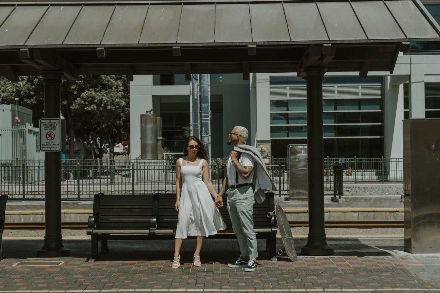 Two people walking together under a covered walkway in front of modern buildings.