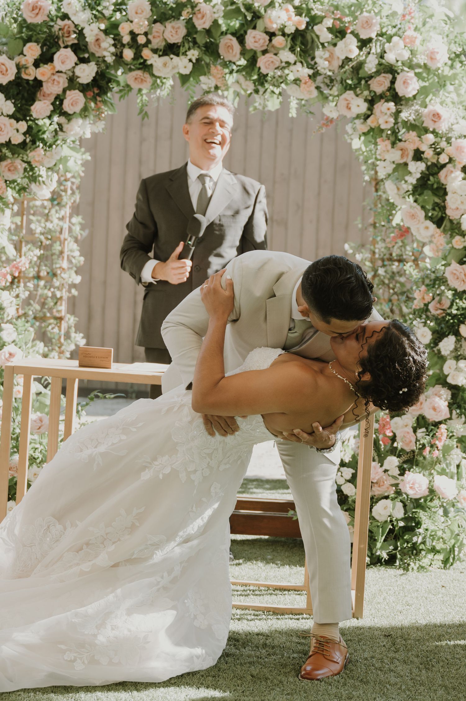 Romantic wedding moment under a floral arch with pink and white roses.