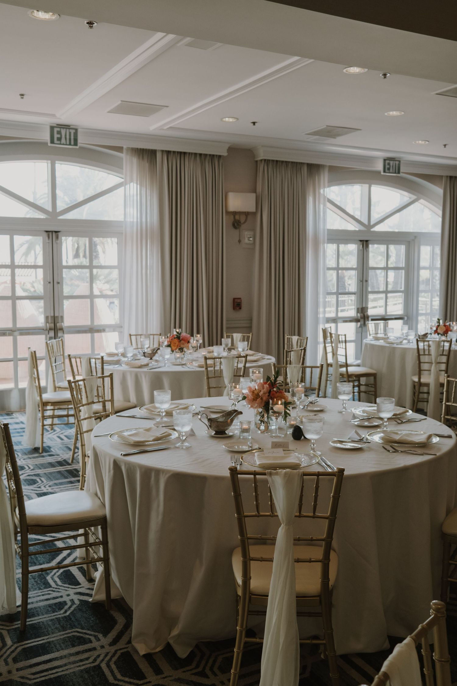 Elegant wedding reception setup with round tables, gold chairs, and white linens.